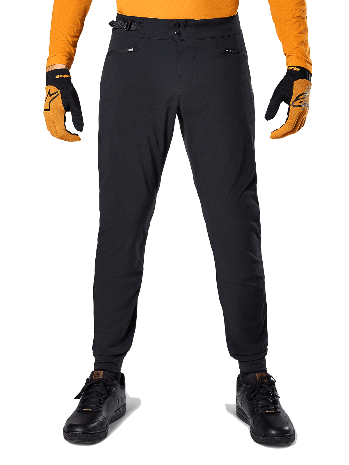 Pantaloni Alpinestars A-Dura, pantaloni da mountain bike, nero, indossati con una maglia arancione a maniche lunghe e guanti neri e arancioni, caratterizzati da una doppia chiusura a scatto e regolatori laterali in vita, in tessuto resistente per il ciclismo fuoristrada
