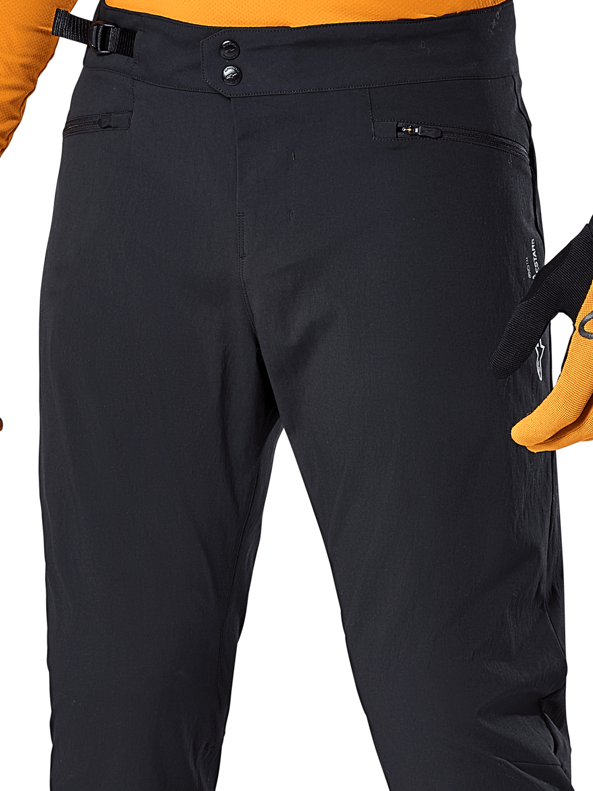 Alpinestars A-Dura Pants, pantaloni da ciclismo MTB neri, vista ravvicinata con doppia chiusura a scatto in vita, regolatore laterale della vita e tasche con cerniera, abbinati a maglia e guanti arancioni