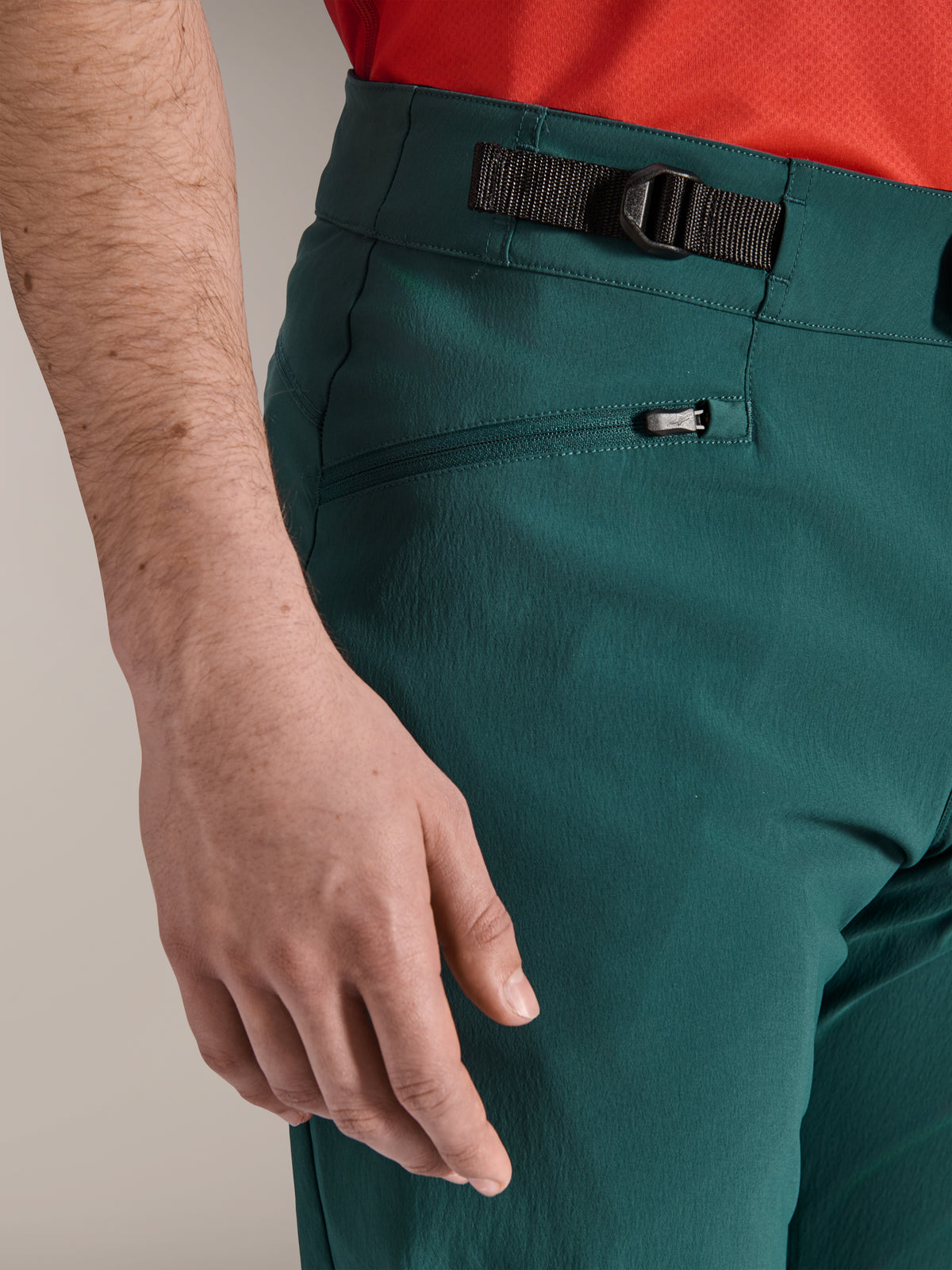 Primo piano dei pantaloni Alpinestars A-Dura in verde Dark Pine, con chiusura laterale regolabile e tasca con cerniera foderata in rete, abbigliamento resistente per mountain bike e trail riding fuoristrada.