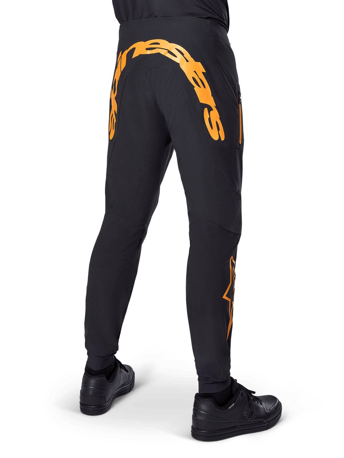 Pantaloni Alpinestars A-Supra Race, pantaloni MTB neri, vista posteriore con grande scritta Alpinestars arancione sul retro, logo arancione sulla parte inferiore della gamba, vestibilità performante con tasca con zip, indossati con scarpe nere