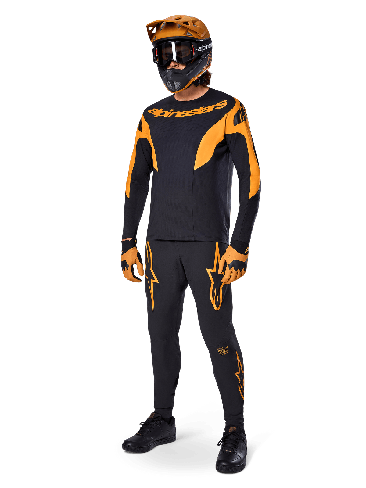 Ciclista di mountain bike con abbigliamento completo da gara, pantaloni Alpinestars A-Supra Race in nero con dettagli arancioni, maglia a maniche lunghe coordinata nera e arancione, casco arancione con maschera nera, guanti arancioni e neri e scarpe nere, design professionale per kit da gara MTB