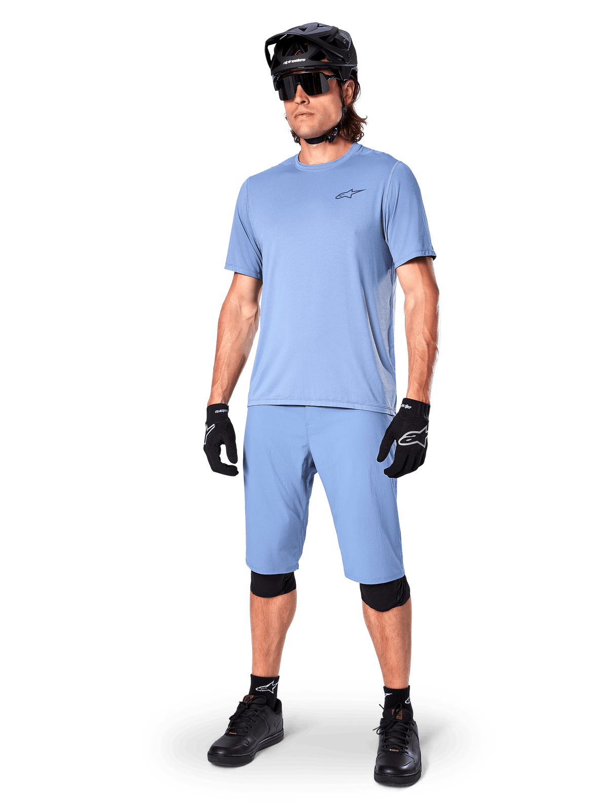 Modello che indossa i pantaloncini Alpinestars A-Dura in Infinity Blue, maglia a maniche corte azzurra coordinata, casco da MTB nero, occhiali da sole e guanti neri, abbigliamento completo da mountain bike per trail riding