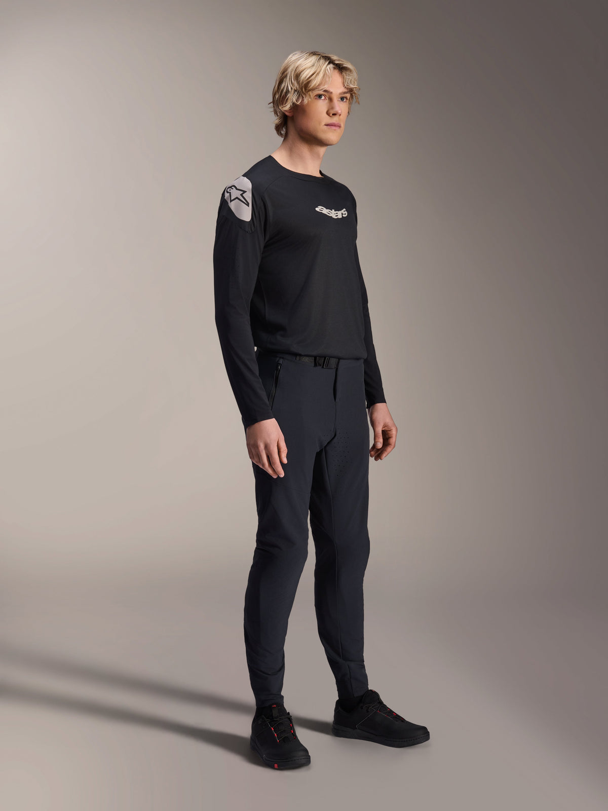Modello che indossa la maglia Alpinestars A-Aria Polartec Elite a maniche lunghe in nero, abbinata a pantaloni tecnici da mountain bike neri coordinati e scarpe nere, abbigliamento da ciclismo performante per il fuoristrada, scatto in studio.