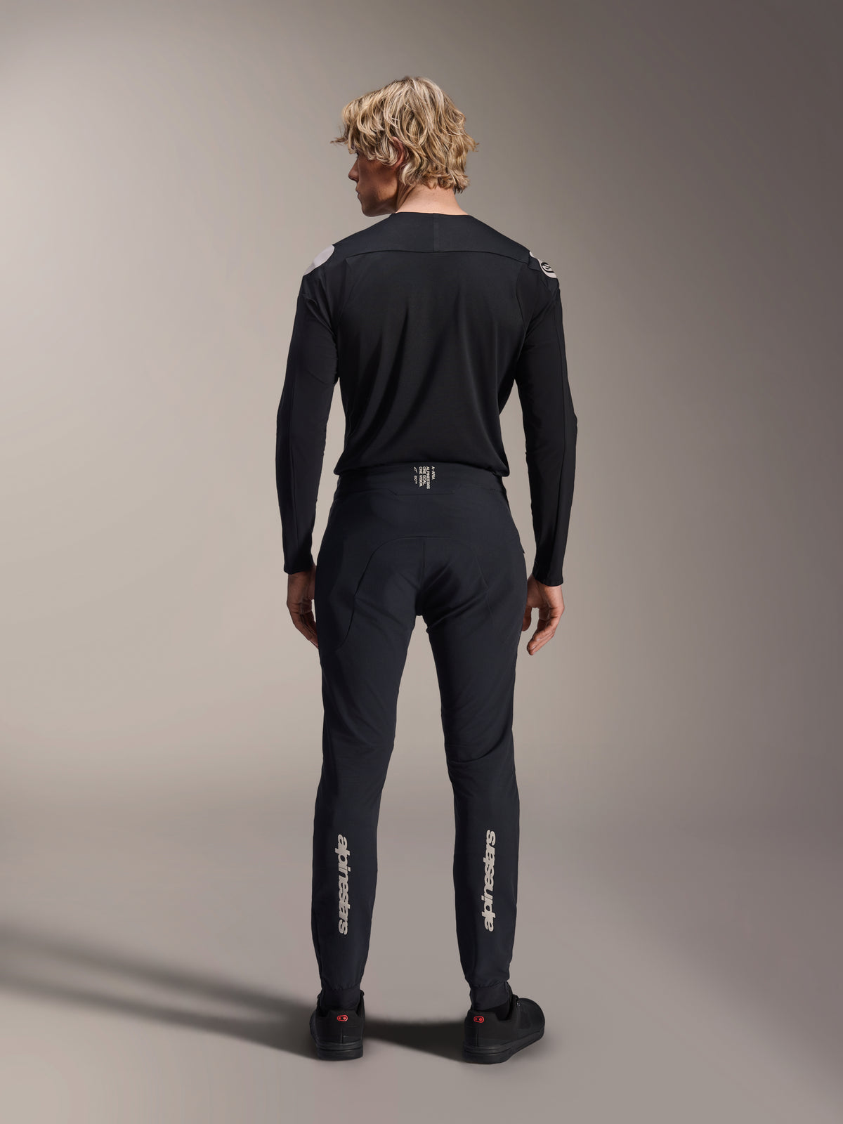 Pantaloni Alpinestars A-Aria Elite, Black Titanium, vista posteriore su modello, con loghi Alpinestars argento sulla parte inferiore delle gambe, pantaloni tecnici da MTB con vestibilità performante e dettaglio della fascia in vita traspirante.