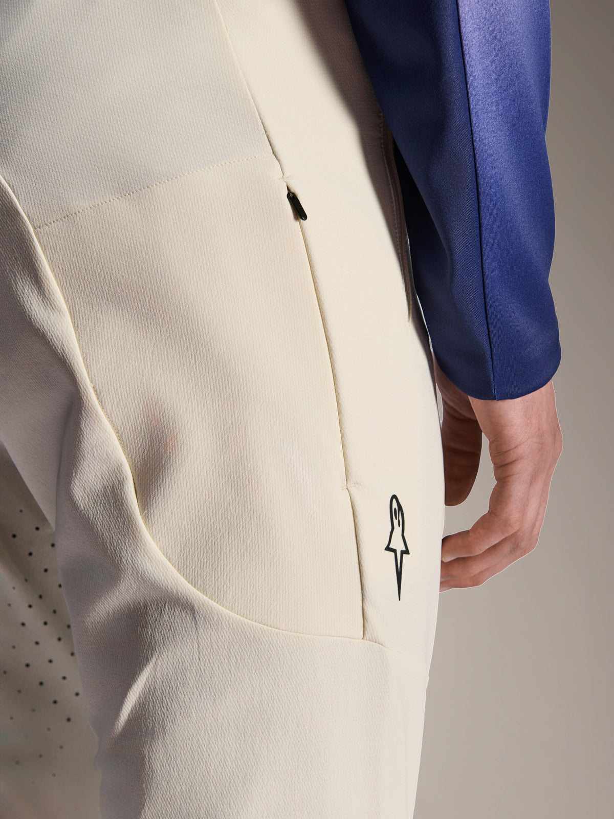 Pantaloni Alpinestars A-Aria Elite, pantaloni tecnici color ecru, vista ravvicinata della tasca laterale con zip e delle perforazioni laser per la ventilazione, dettaglio del logo minimalista, tessuto ad alta elasticità per mountain bike