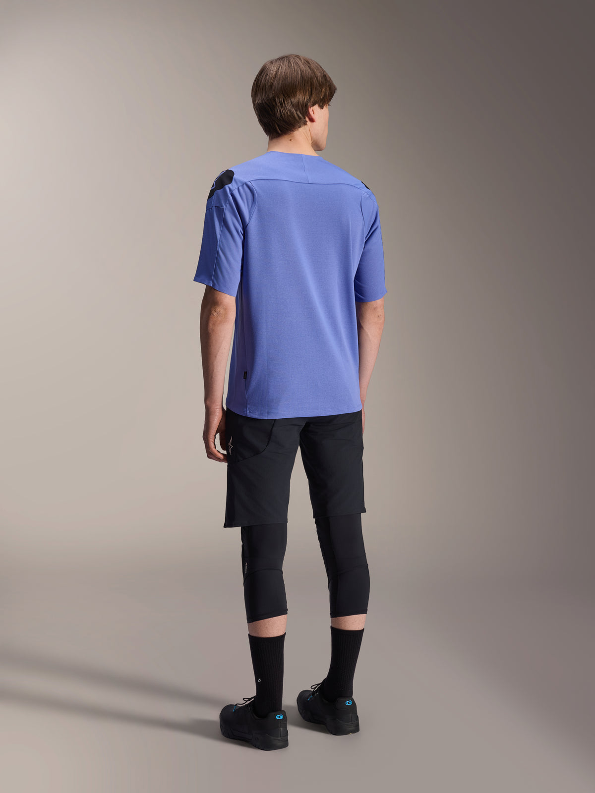 Alpinestars A-Aria Elite Shorts, pantaloncini da mountain bike, Black Titanium, vista posteriore indossati con maglia a maniche corte color lavanda, ginocchiere nere e scarpe da ciclismo nere, completo tecnico da MTB.