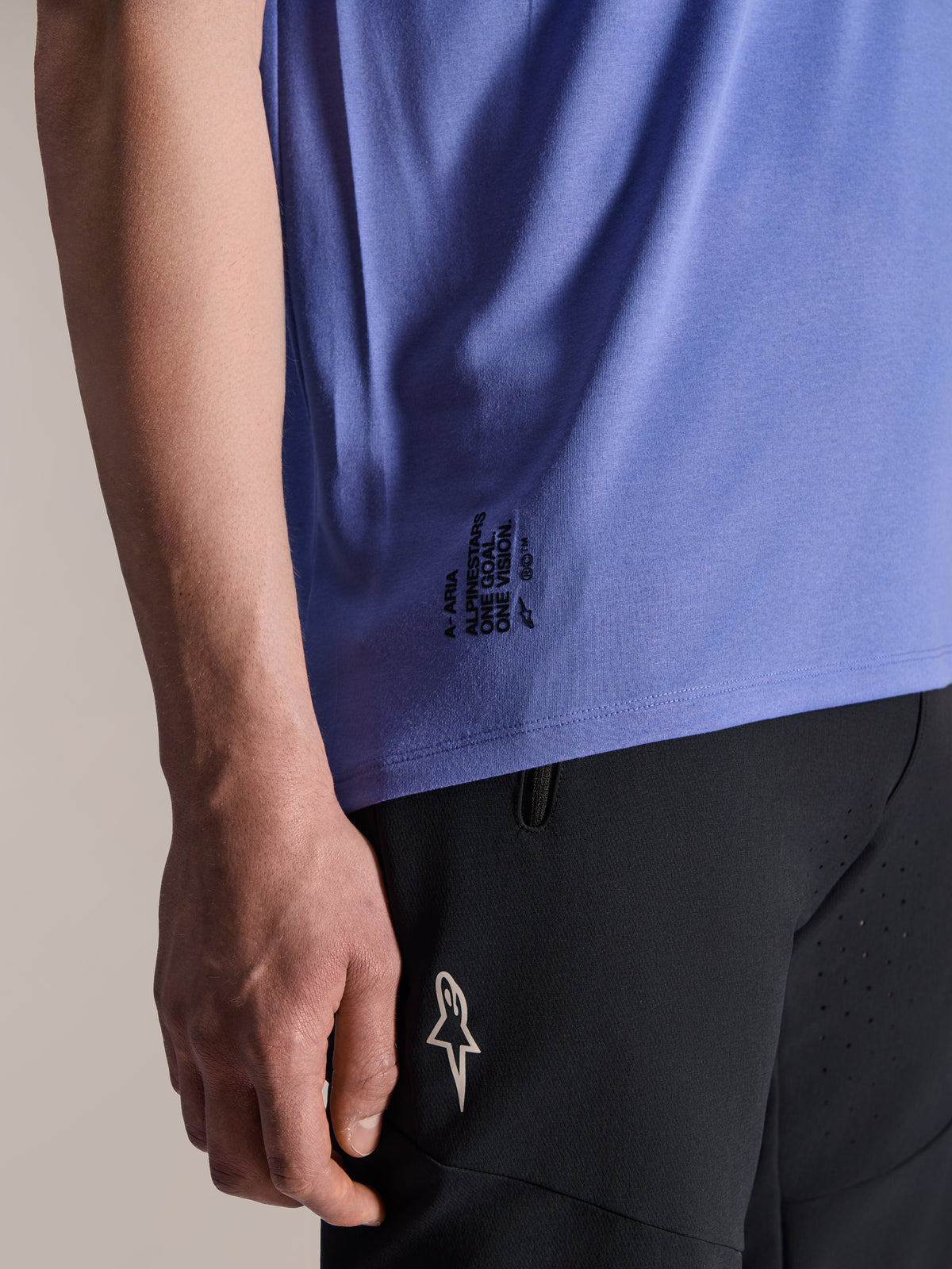 Maglia a maniche corte Alpinestars A-Aria Polartec Elite in Baja Blue, dettaglio dell'orlo laterale inferiore con la scritta nera 'One Goal. One Vision.' e il logo ASTARS, abbinata a pantaloncini neri da mountain bike.