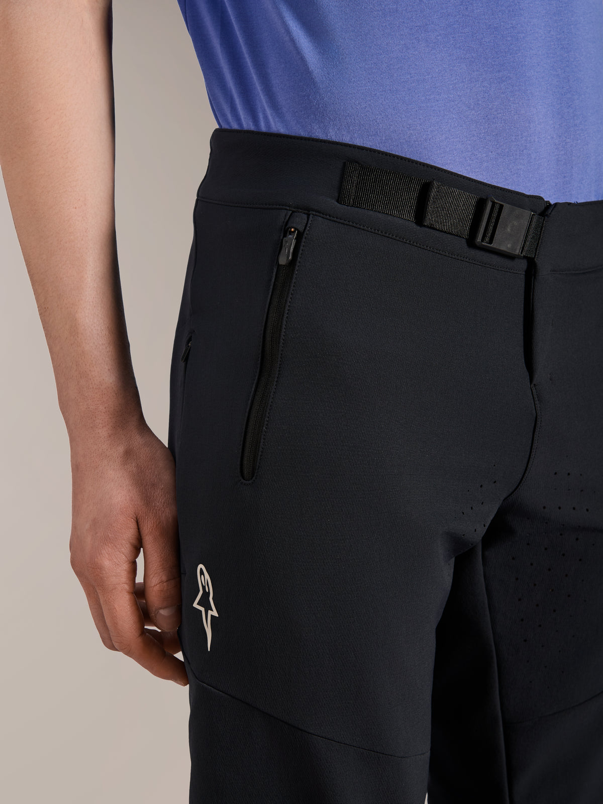 Alpinestars A-Aria Elite Shorts, pantaloncini da mountain bike, Black Titanium, con chiusura a fibbia magnetica, tasca con zip e logo Alpinestars bianco, indossati con una maglia da ciclismo blu, abbigliamento tecnico da mountain bike