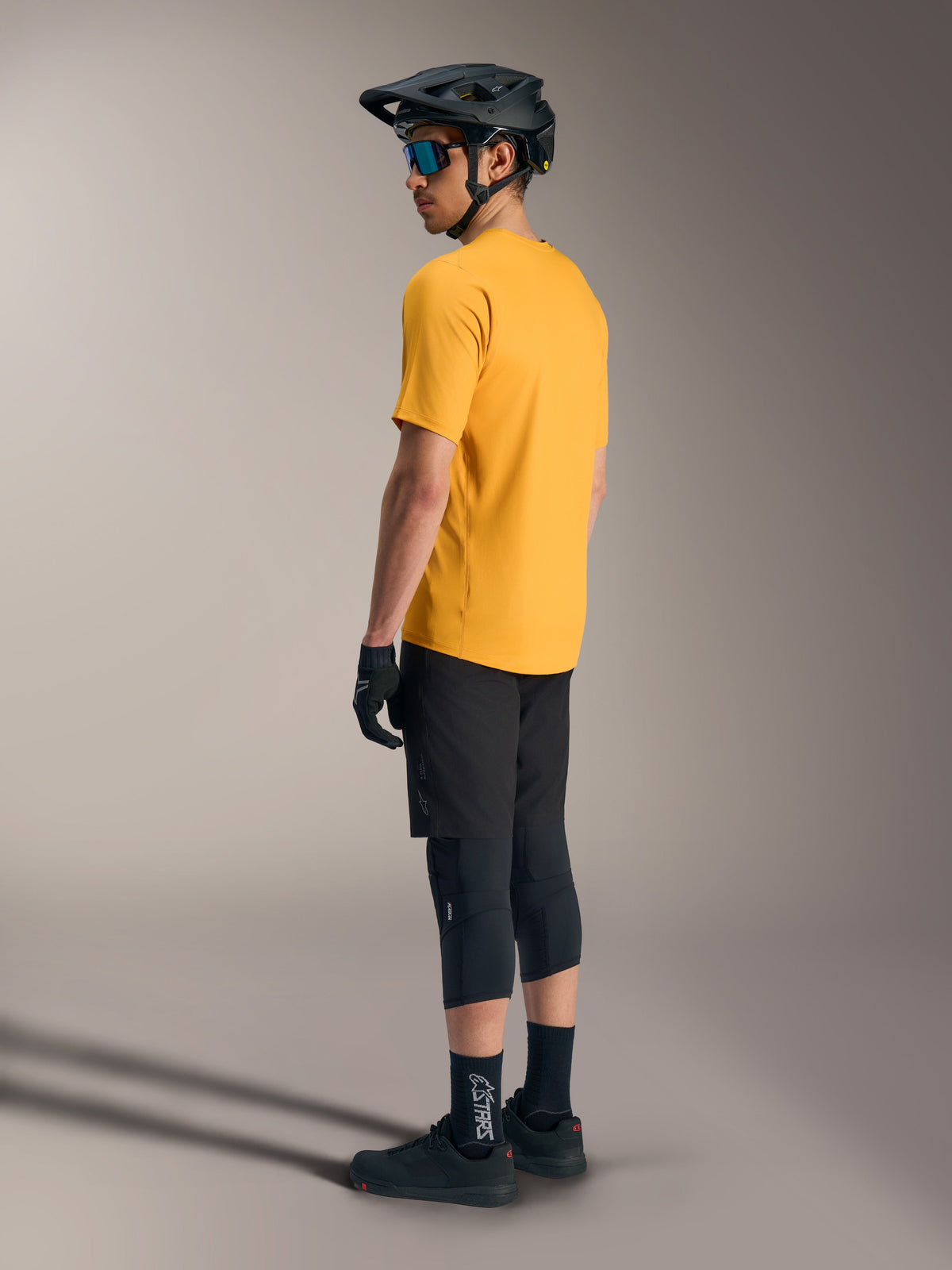 Maglia Alpinestars A-Dura Ride arancione a maniche corte, vista posteriore con casco e attrezzatura MTB nera.