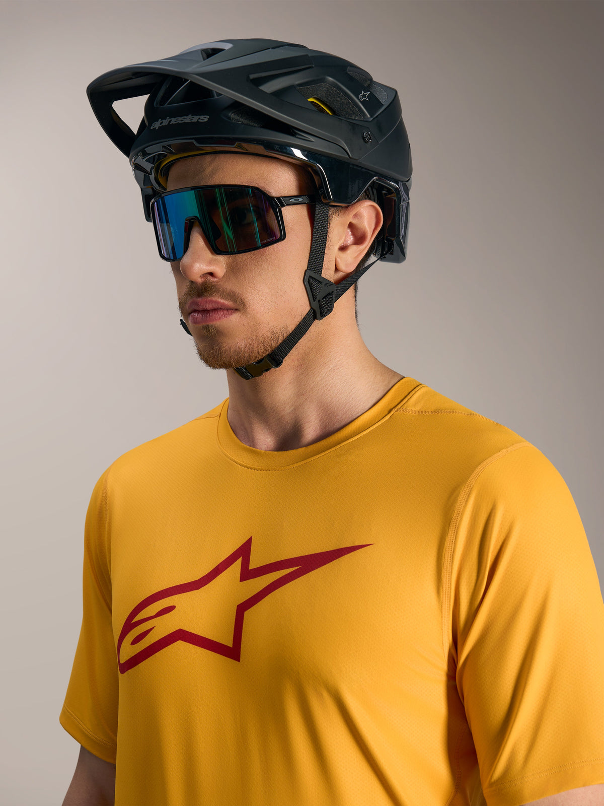 Maglia A-Dura Ride arancione con logo Astars rosso, casco MTB nero e occhiali tecnici, abbigliamento cycling Alpinestars.