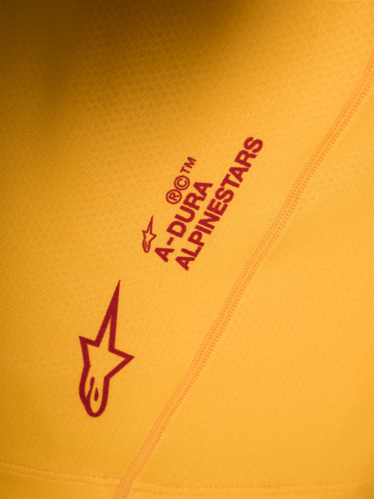 Maglia Alpinestars A-Dura Ride arancione, dettaglio del logo Astars rosso e scritta stampati su tessuto tecnico elasticizzato.