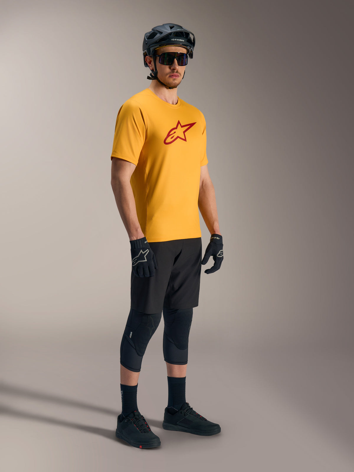 Maglia A-Dura Ride arancione con logo Astars rosso, abbinata a casco e attrezzatura tecnica da MTB neri.