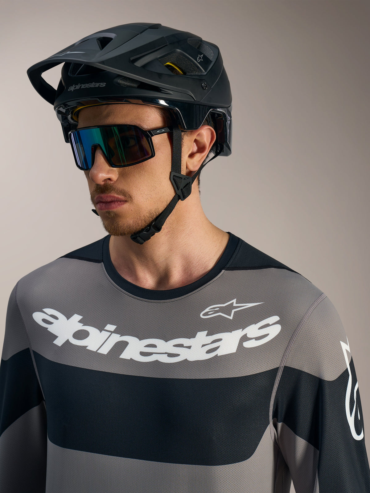 Maglia Alpinestars A-Dura Race a maniche lunghe grigia con loghi bianchi, casco da MTB nero e occhiali da sole tecnici.