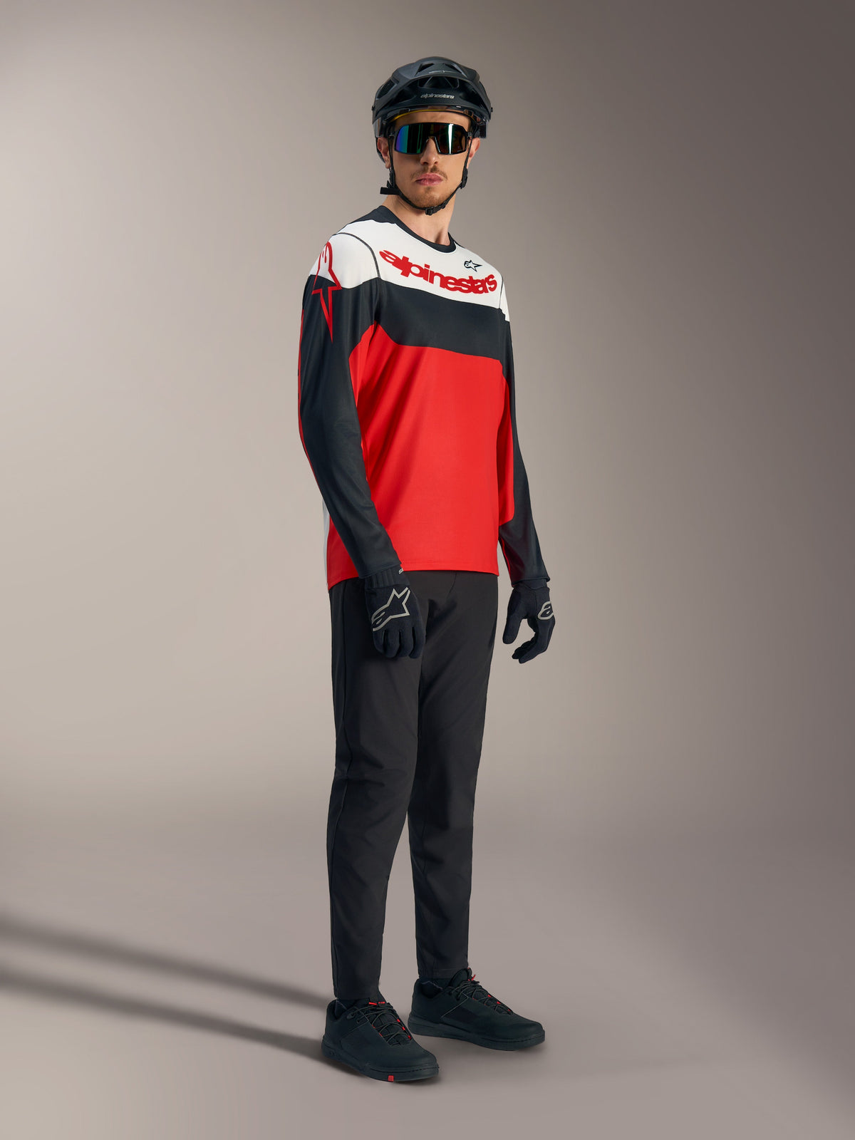 Maglia Alpinestars A-Dura Race rossa, nera e bianca con loghi audaci, abbinata a attrezzatura professionale da MTB.