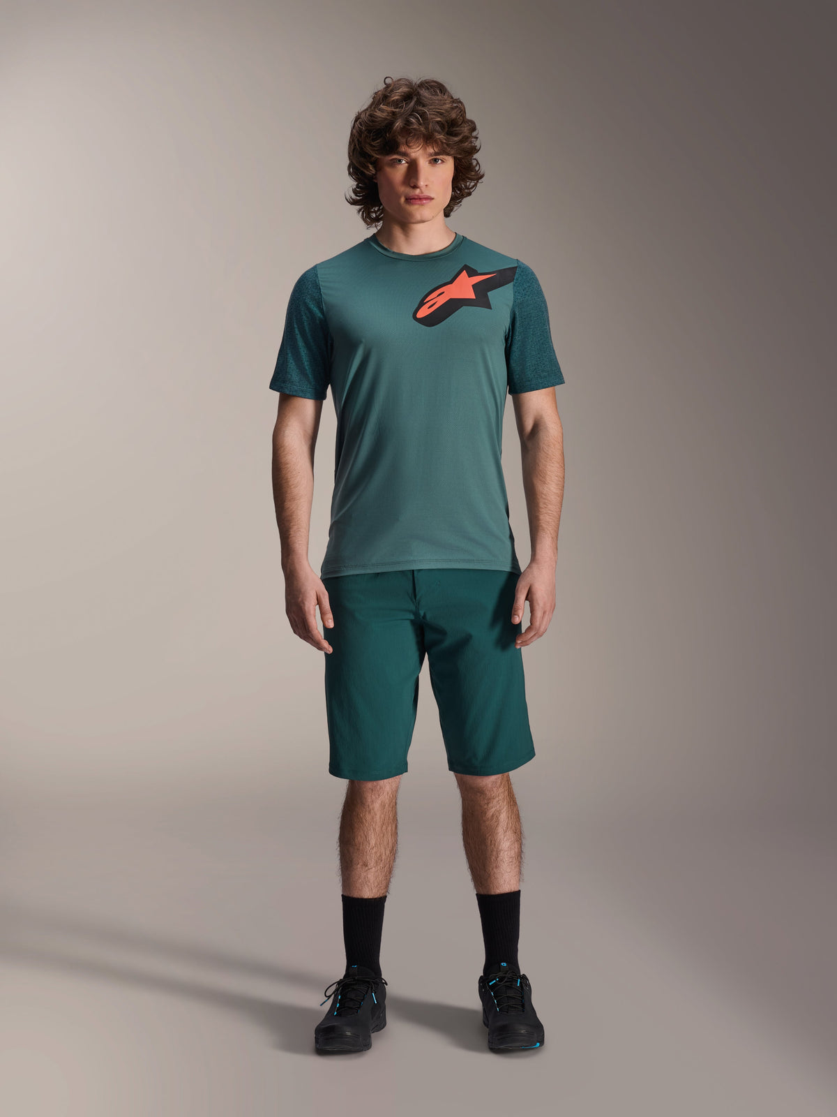 Alpinestars A-Dura Lipan Jersey, maglia da MTB a maniche corte, verde Silver Pine con logo Astars nero e arancione sul petto, abbinata a pantaloncini coordinati e scarpe nere, abbigliamento tecnico da mountain bike