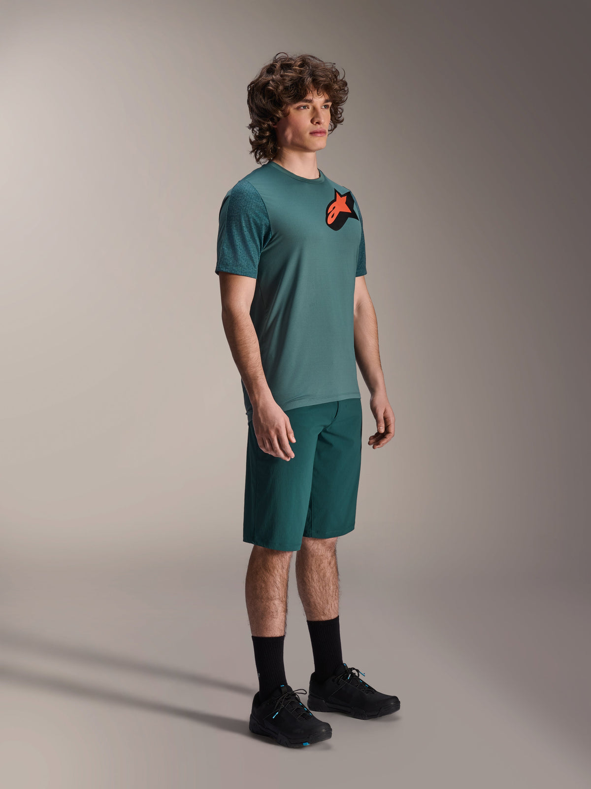 Maglia Alpinestars A-Dura Lipan, maglia MTB a maniche corte, colore Silver Pine, con logo Astars arancione e nero sul petto, indossata con pantaloncini verdi abbinati e scarpe da ciclismo nere, stile trail casual