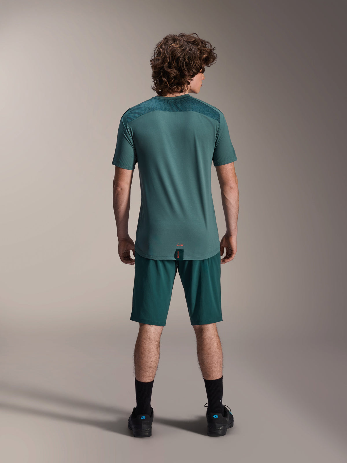 Maglia Alpinestars A-Dura Lipan a maniche corte in Silver Pine, vista posteriore che mostra i pannelli in jacquard sulle spalle e l'orlo posteriore allungato, indossata con pantaloncini da mountain bike verde scuro coordinati e calzature nere.