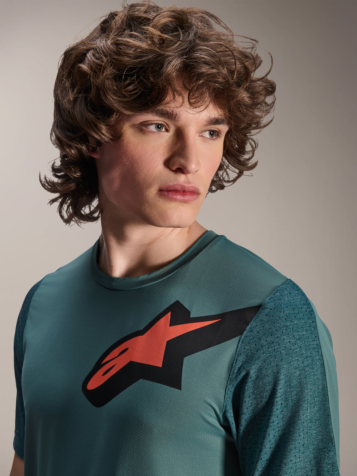 Alpinestars A-Dura Lipan Jersey, maglia MTB a maniche corte, Silver Pine, con prominente logo Astars rosso e nero sul petto, maniche in jacquard testurizzato, ritratto ravvicinato di un modello che indossa abbigliamento tecnico da ciclismo