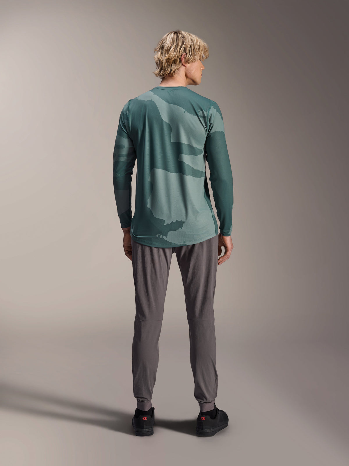 Alpinestars A-Dura Hollow Camo Jersey - Manica Lunga, motivo mimetico verde Silver Pine Camo, indossata da un modello vista da dietro con pantaloni tecnici grigi, abbigliamento tecnico per mountain bike
