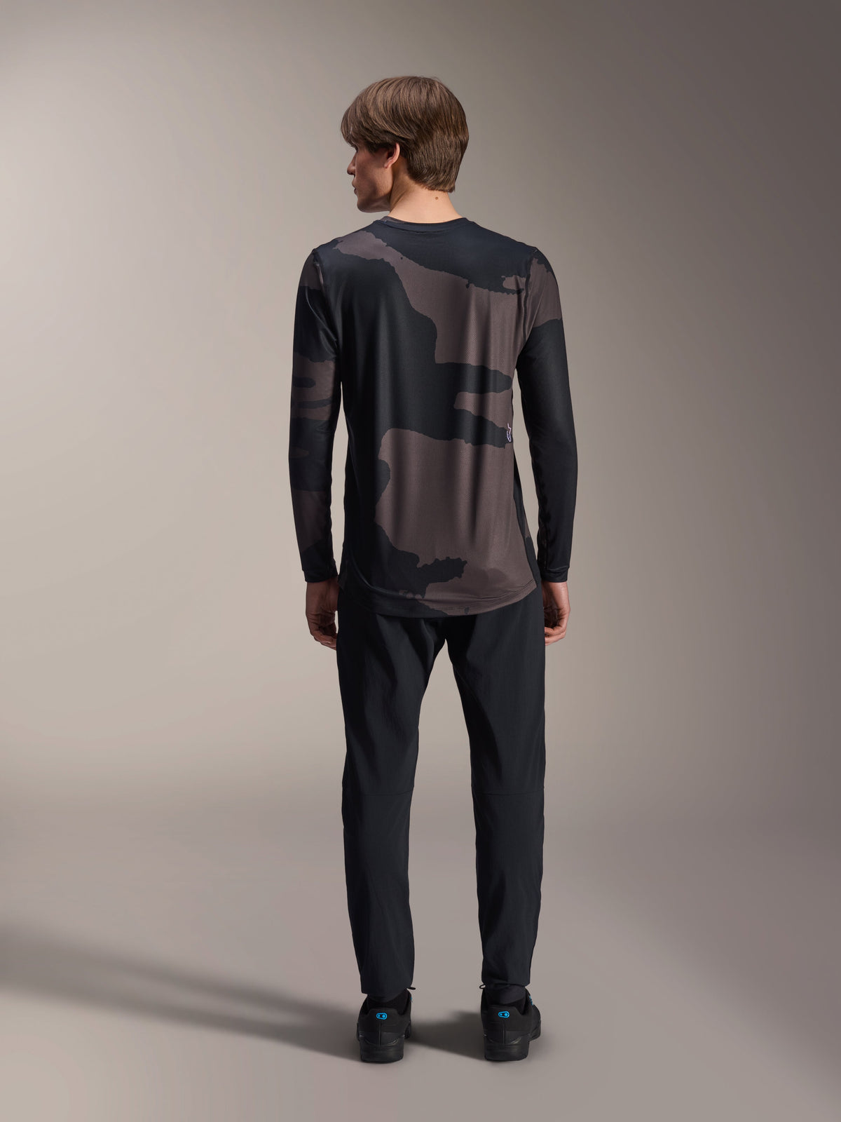 Alpinestars Maglia A-Dura Hollow Camo a maniche lunghe, Black Camo, vista posteriore indossata con pantaloni neri, motivo camouflage scuro e orlo posteriore allungato per maggiore copertura MTB