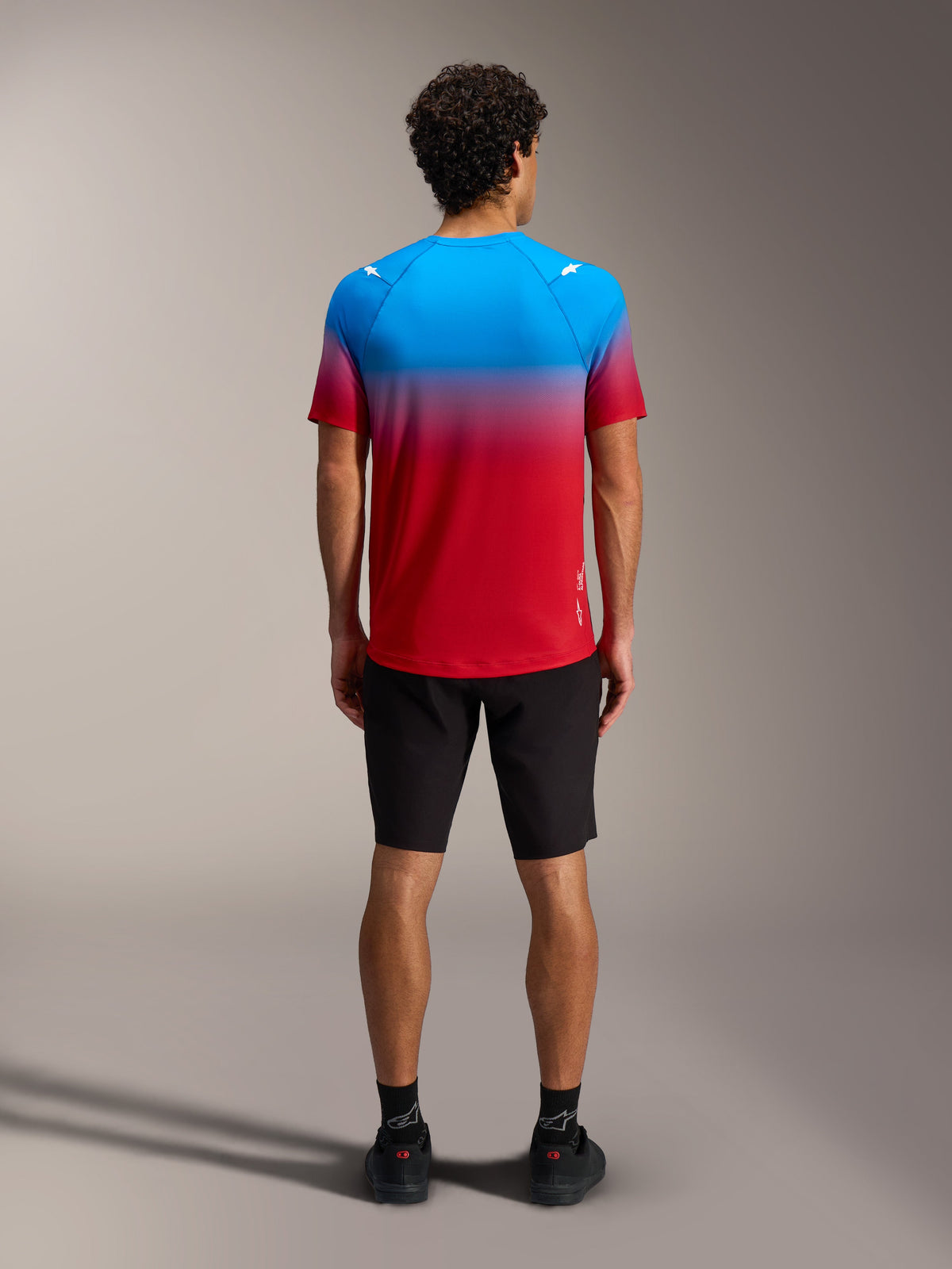 Maglia MTB A-Dura ASTARS 2.0 con sfumatura rosso e blu, maniche corte, vista posteriore con pantaloncini neri.