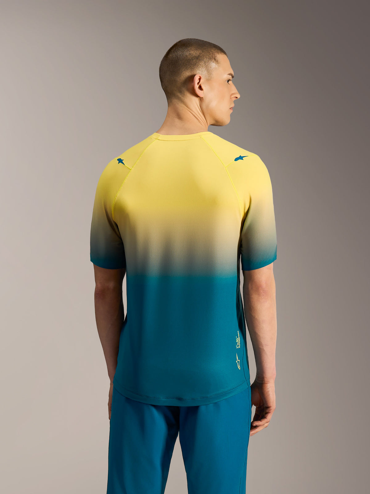 Maglia MTB Alpinestars A-Dura ASTARS 2.0 a maniche corte, design tecnico sfumato giallo e blu-verde visto dal retro.