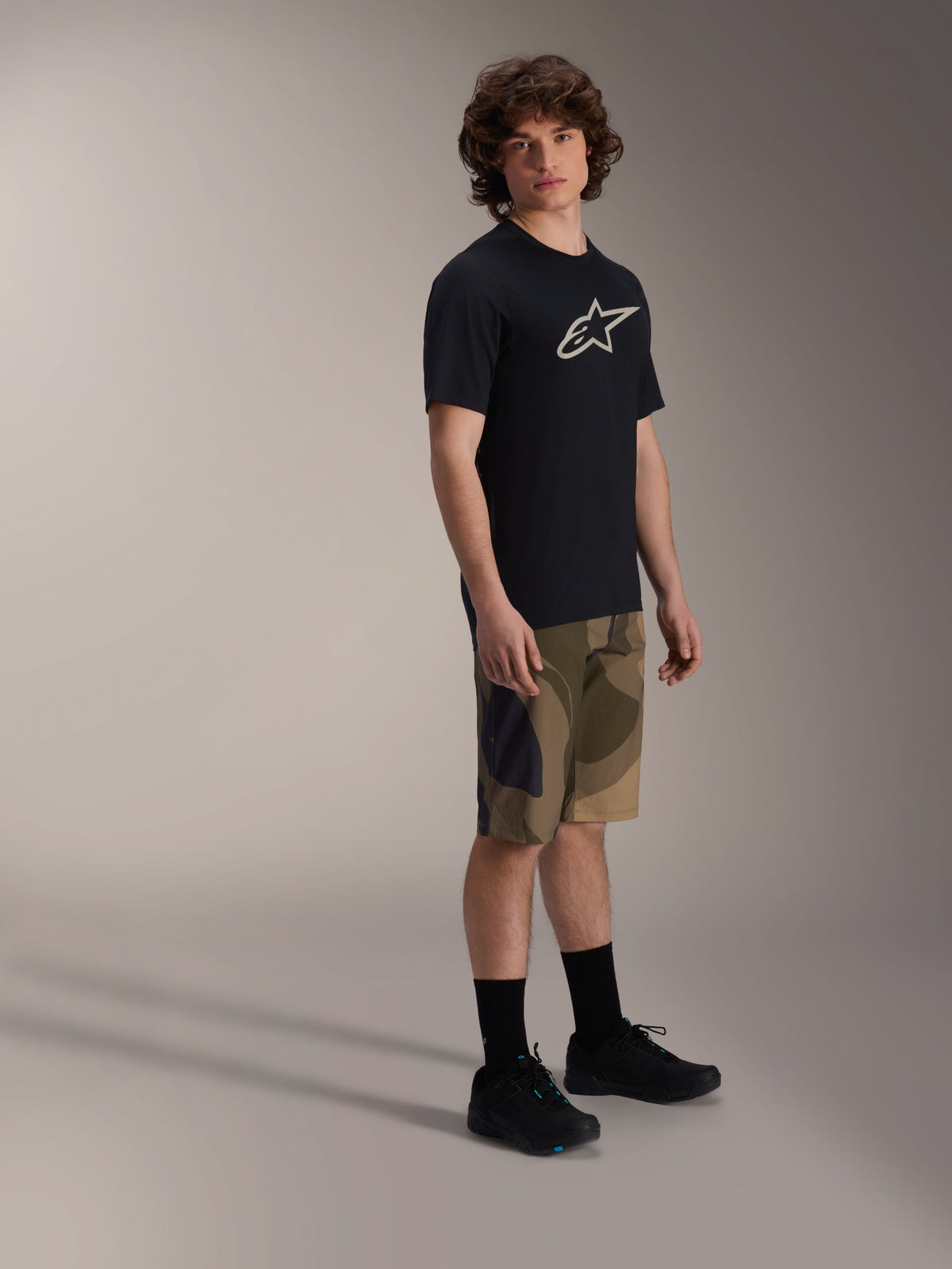 Alpinestars Maglia A-Dura Astar a maniche corte, nera con logo bianco sul petto, indossata con pantaloncini camouflage e scarpe da MTB nere, abbigliamento casual per mountain bike