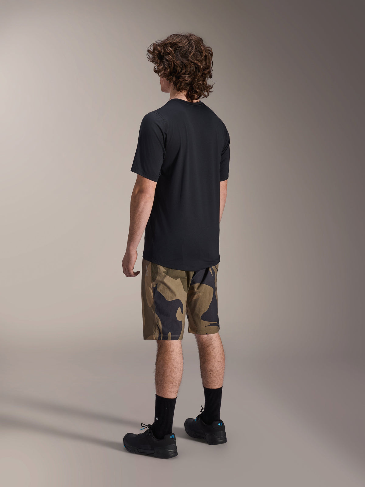Maglia Alpinestars A-Dura Astar a maniche corte in nero, vista dal retro, abbinata a pantaloncini camouflage, calze e scarpe sportive nere, abbigliamento casual da MTB