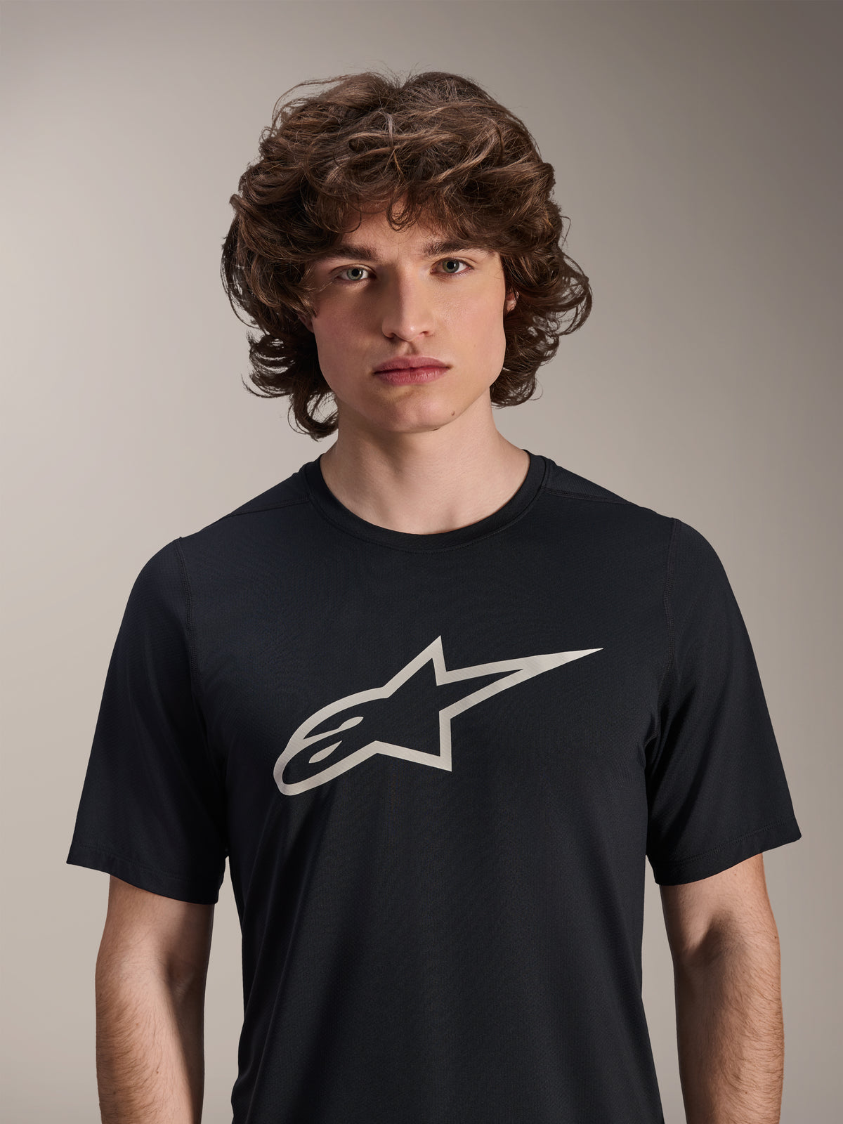 Alpinestars Maglia A-Dura Astar a maniche corte, nera, con un grande logo Astar bianco sul petto, indossata da un modello, abbigliamento tecnico casual per mountain bike