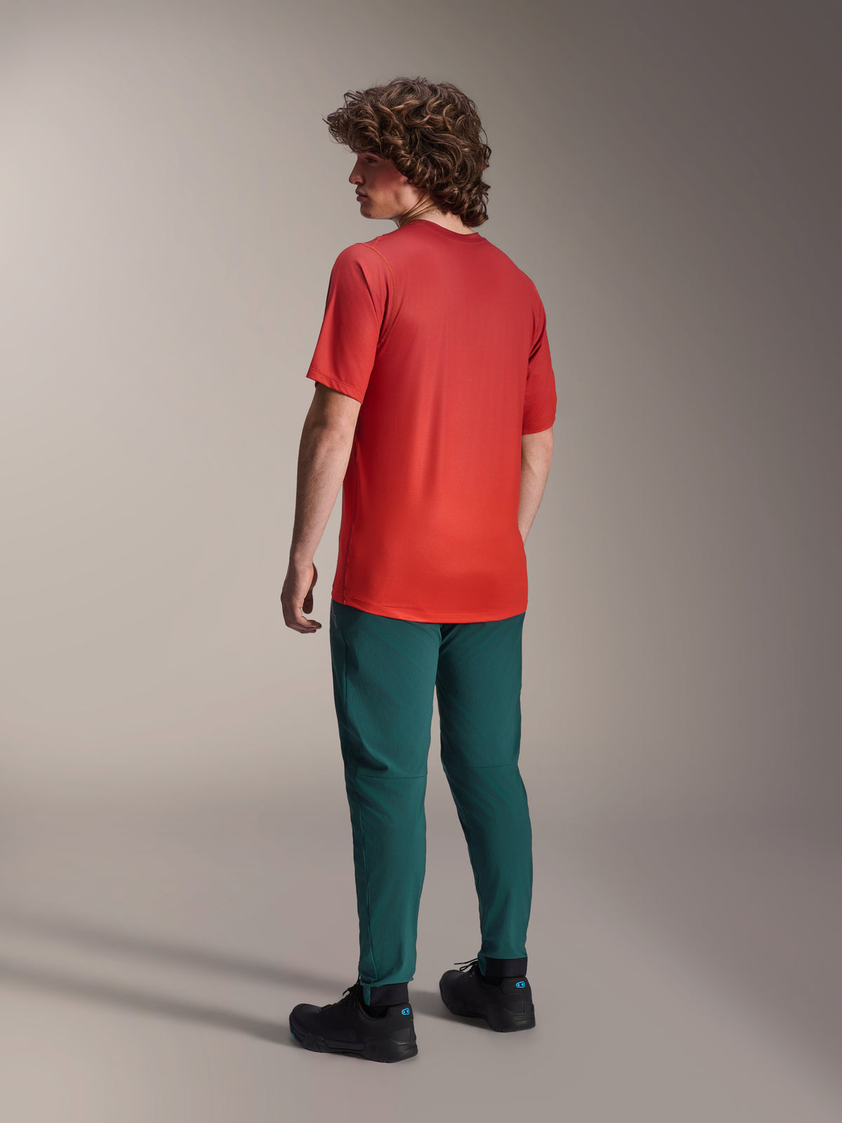 Modello visto da dietro che indossa pantaloni Alpinestars A-Dura in verde Dark Pine e una maglia a maniche corte A-Dura Rise rossa, con vestibilità regolare e polsini elasticizzati, abbigliamento tecnico da mountain bike per il fuoristrada