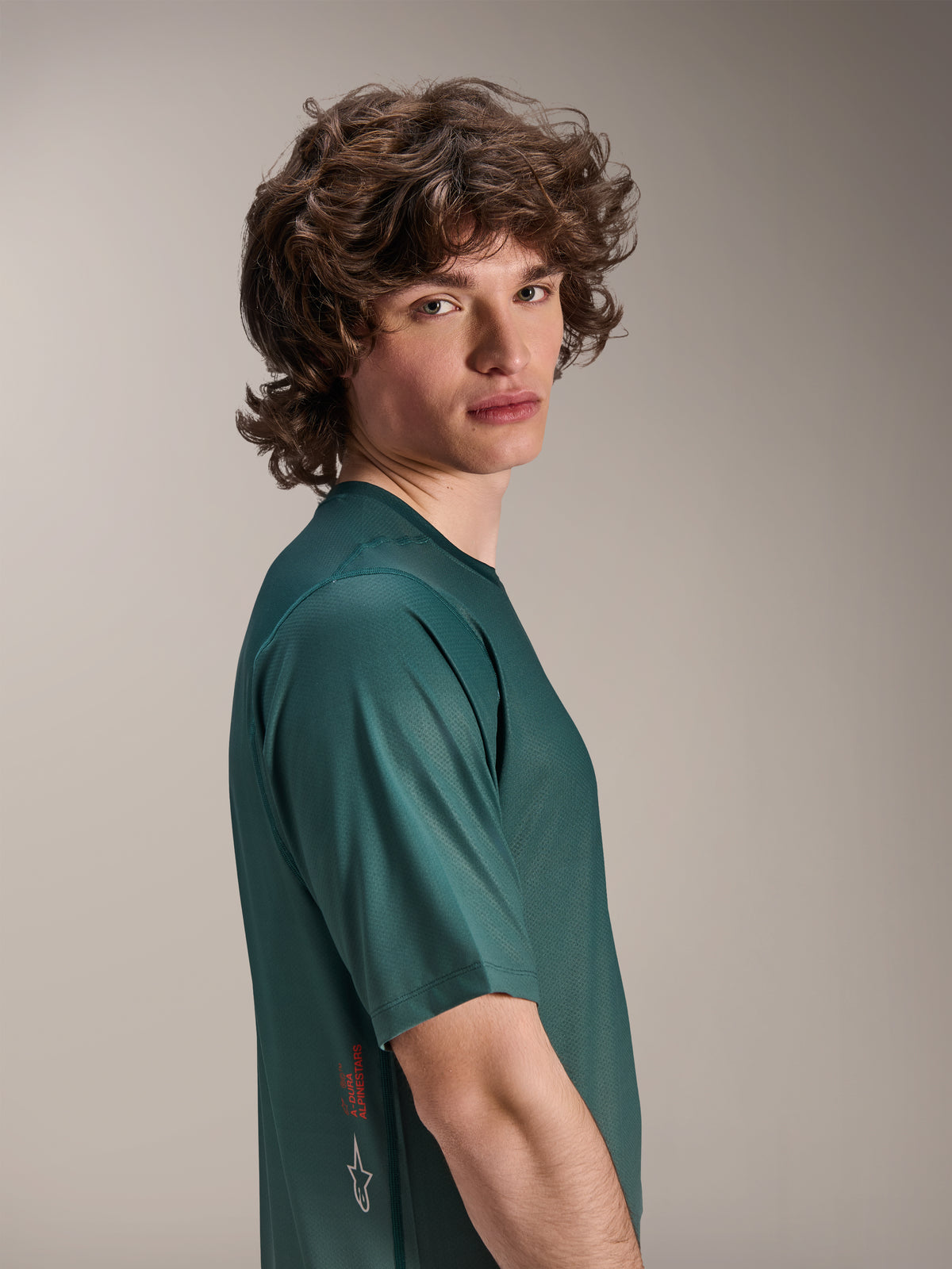 Alpinestars A-Dura Rise Jersey, maglia MTB a maniche corte, verde Silver Pine, modello che indossa il tessuto jacquard traspirante, scritta A-Dura Alpinestars rossa e logo bianco sul lato, abbigliamento tecnico da trail