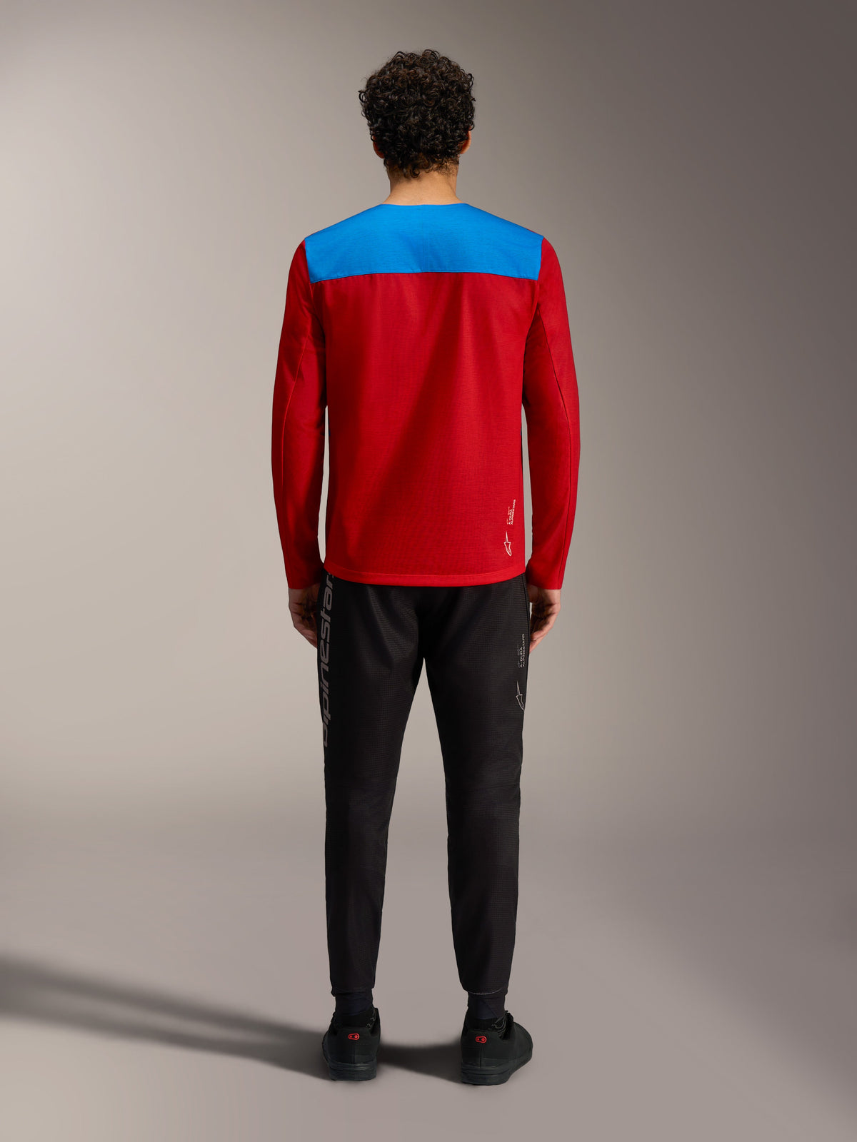 Maglia MTB maniche lunghe Alpinestars A-Dura Elite 2.0 rossa e blu, vista dal retro con pantaloni neri.