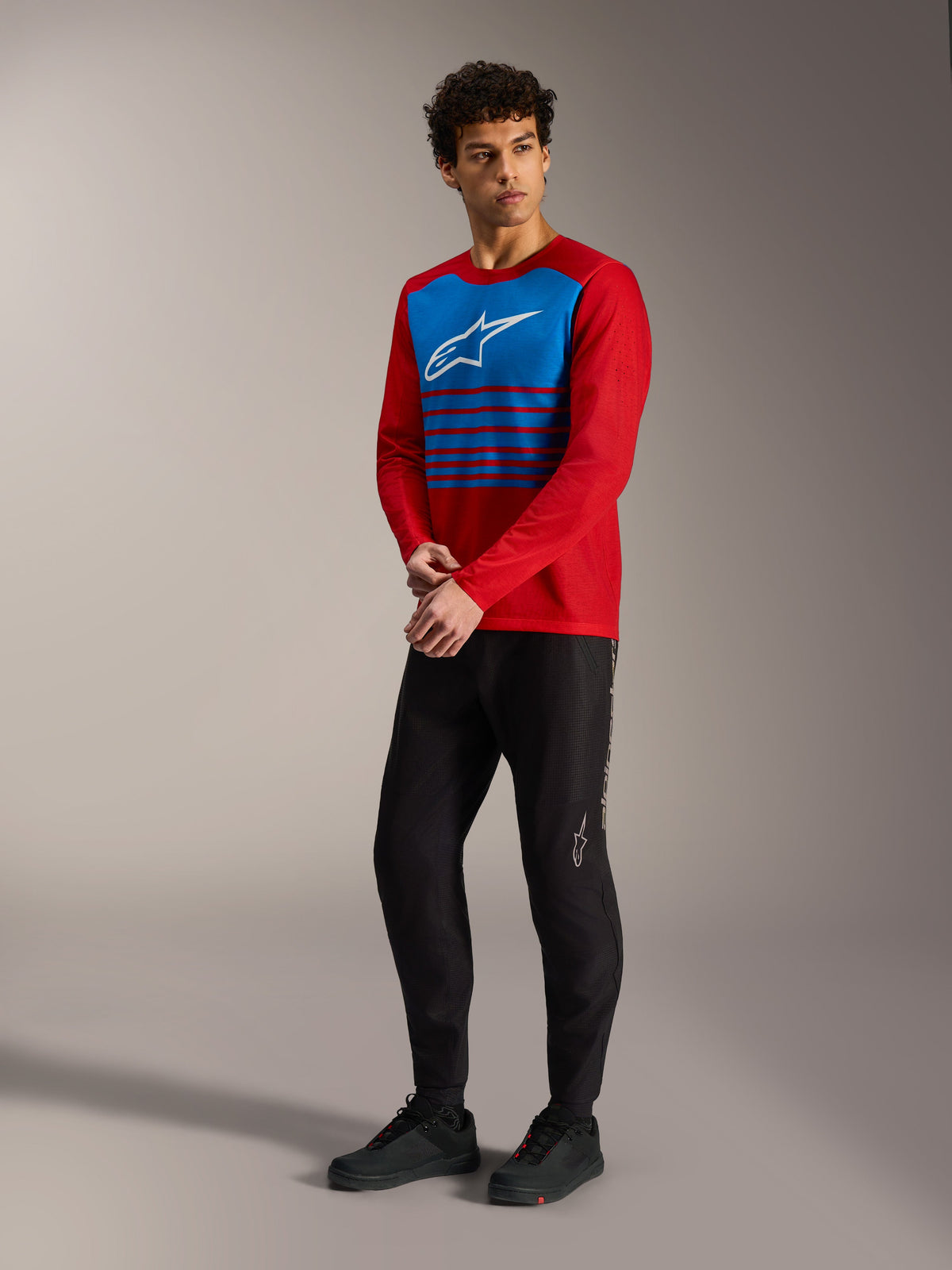 Maglia A-Dura Elite 2.0 rossa a maniche lunghe con pannello blu a righe e logo bianco, abbinata a pantaloni MTB neri.