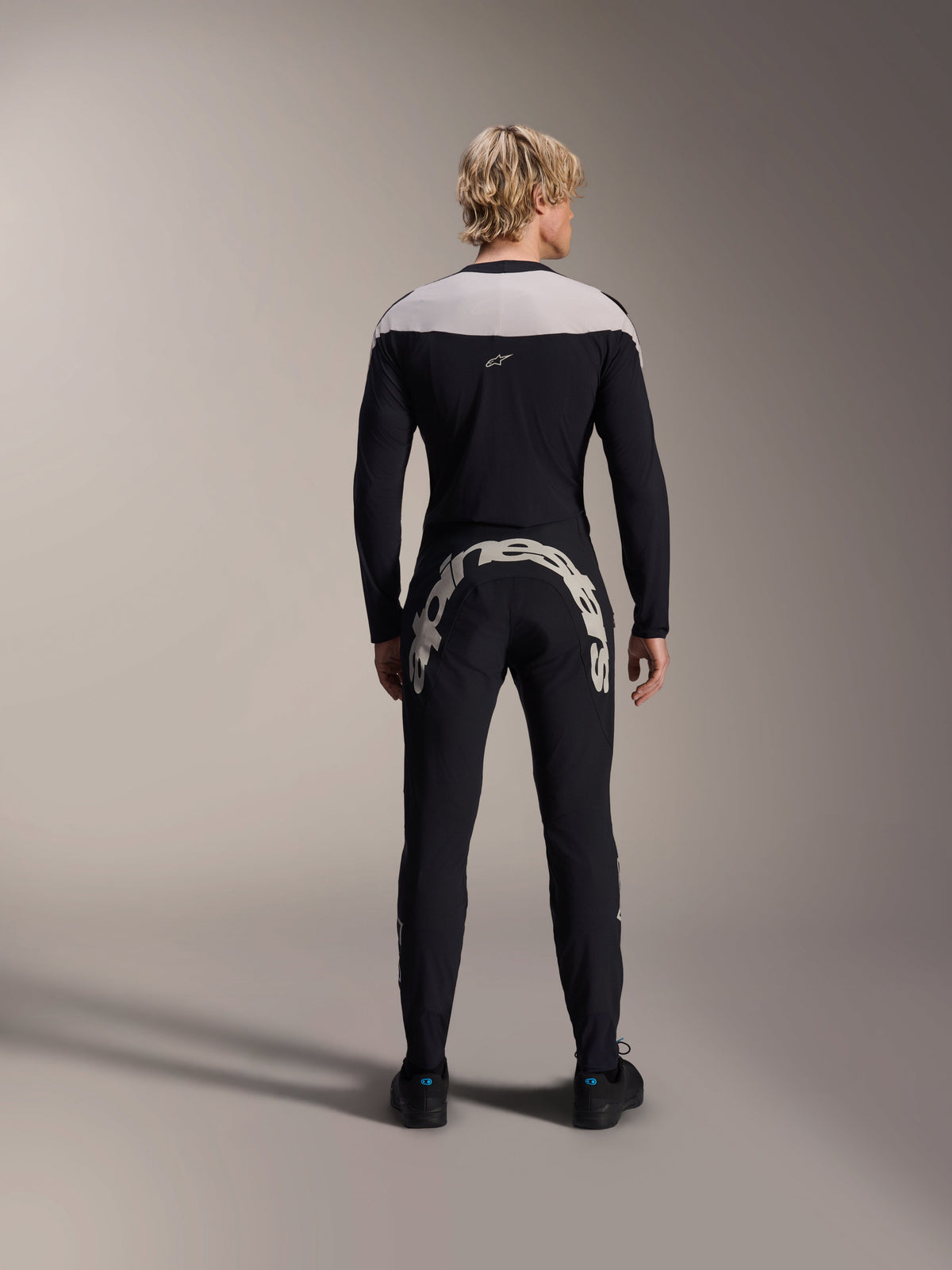 Pantaloni Alpinestars A-Supra Melt, nero, vista posteriore che mostra la grande scritta Alpinestars bianca sul carré posteriore, abbinati a una maglia a maniche lunghe coordinata e scarpe da ciclismo nere, abbigliamento da mountain bike ad alte prestazioni per il fuoristrada