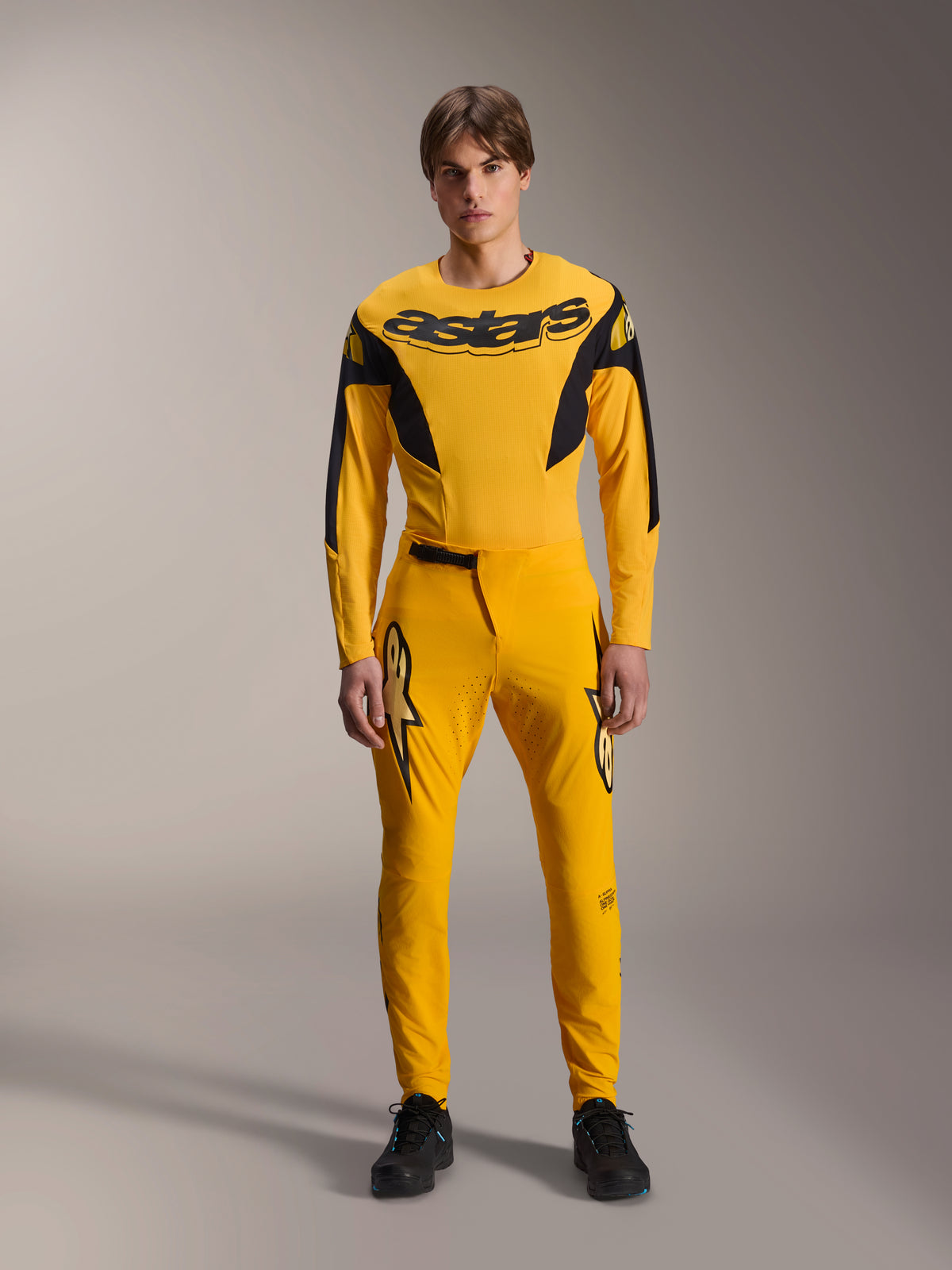 Set completo Limited Edition A-Supra Melt Gold, abbigliamento Mountain Bike Alpinestars, giallo scuro e nero, modello che indossa maglia a maniche lunghe con vistoso logo 'astars' sul petto e pantaloni tecnici coordinati, con ventilazione tagliata al laser sull'interno coscia e chiusura della vita a cricchetto, kit da gara professionale per MTB