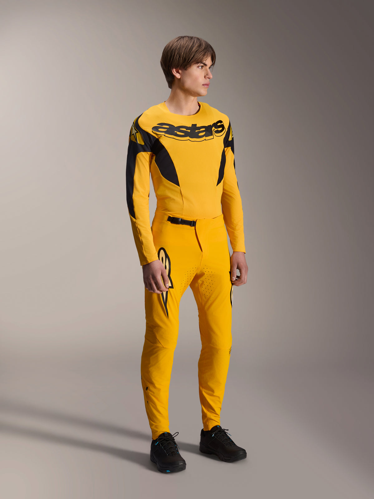 Modello che indossa il set Alpinestars Limited Edition A-Supra Melt Gold, maglia MTB a maniche lunghe gialla con vistoso marchio nero sul petto, pantaloni gialli coordinati con ventilazione laser e dettagli neri, kit completo da gara per mountain bike.