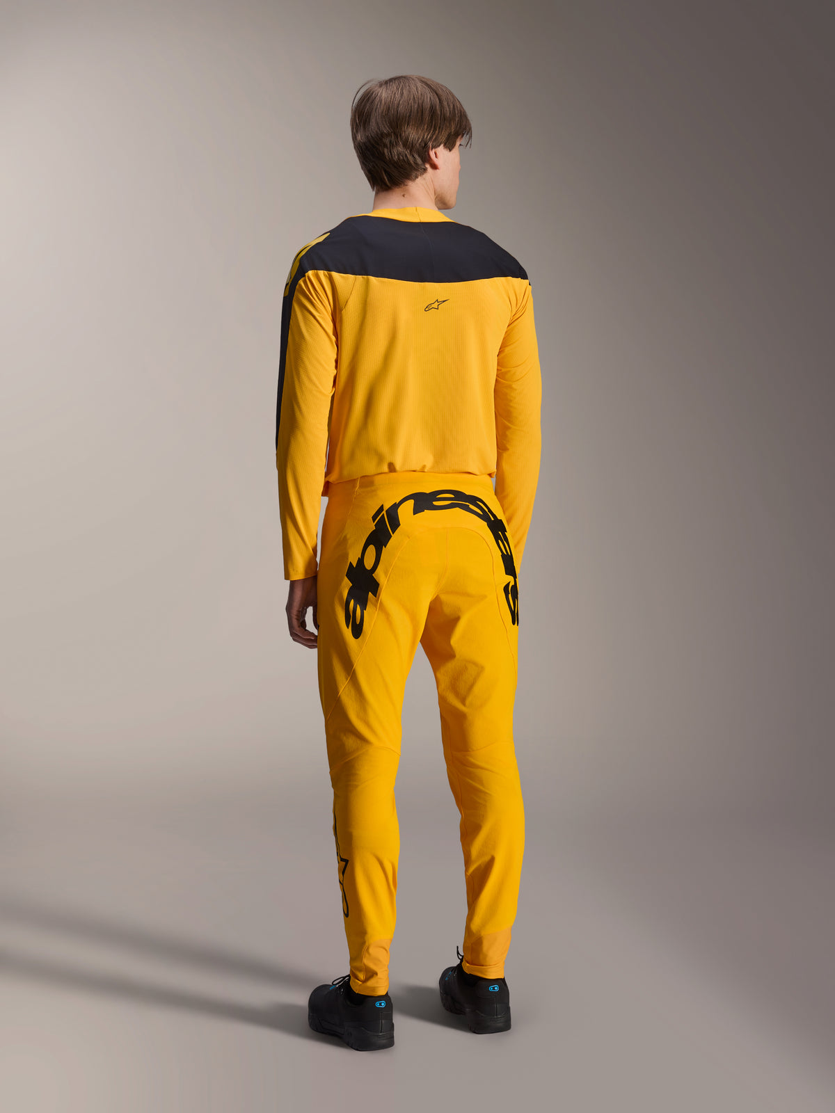 Set abbigliamento Alpinestars Limited Edition A-Supra Melt Gold, maglia e pantaloni da MTB, giallo scuro e nero, vista posteriore con grande scritta Alpinestars sulla seduta e carré nero sulla maglia, abbigliamento tecnico per mountain bike