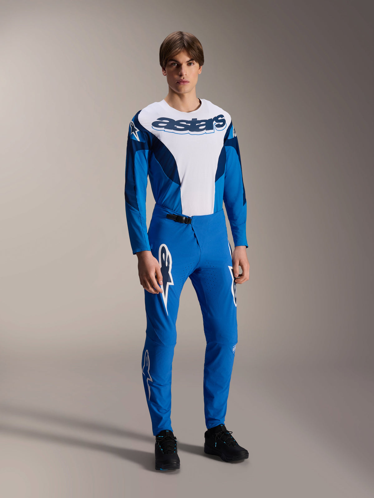 Modello che indossa la maglia Alpinestars A-Supra Melt - Long Sleeve in blu e bianco, caratterizzata da un vistoso logo 'astars' sul petto, abbinata a pantaloni da mountain bike blu coordinati e calzature nere, abbigliamento da gara MTB orientato alle prestazioni.