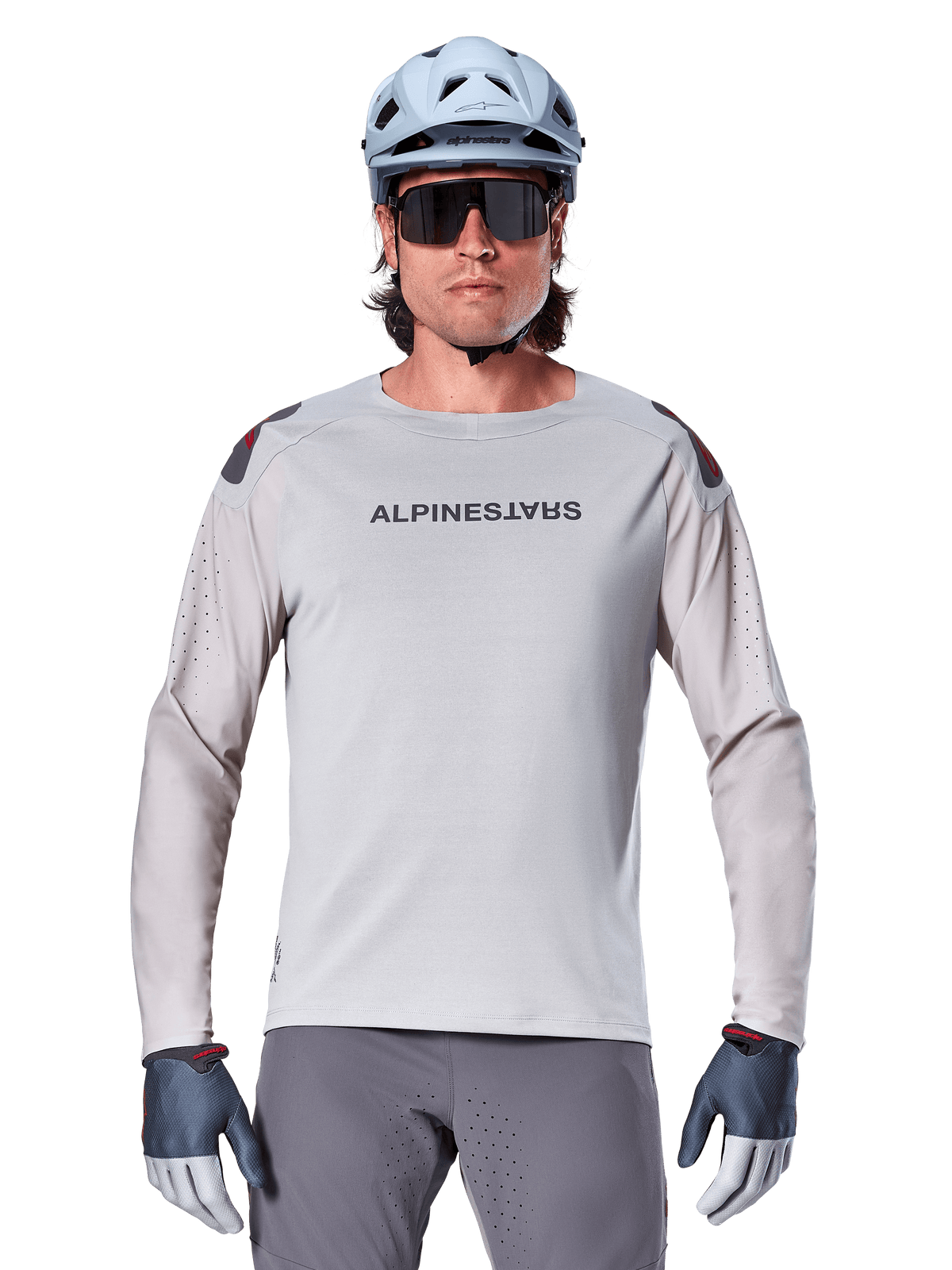 Alpinestars A-Aria Polartec Switch Long Sleeve Jersey, maglia da mountain bike grigio chiaro con perforazioni laser sulle maniche e logo sul petto, indossata con casco celeste, occhiali da sole e guanti grigi