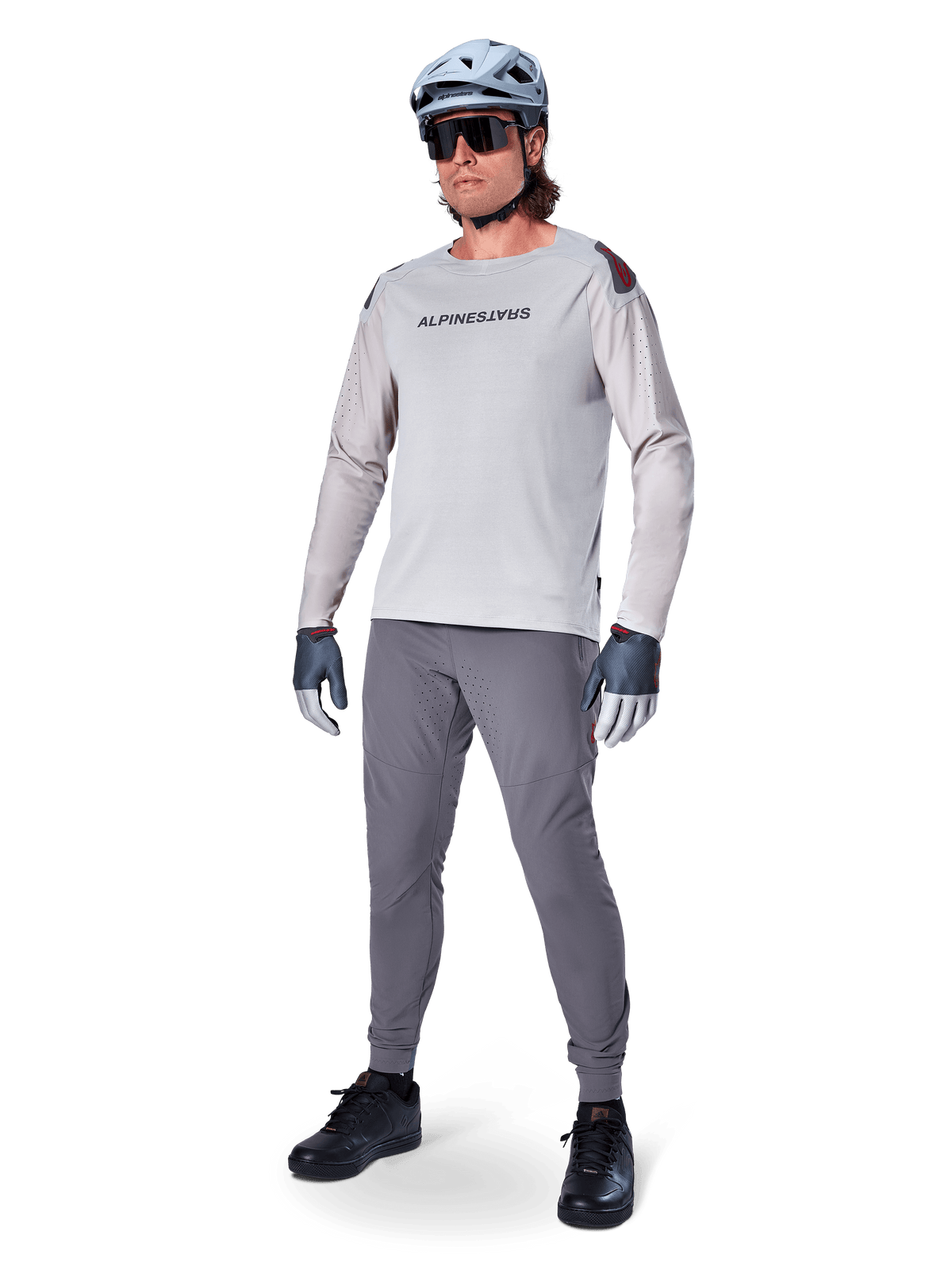 Alpinestars A-Aria Polartec Switch Jersey, maglia da MTB a maniche lunghe, grigio chiaro, indossata con pantaloni da mountain bike grigio scuro, casco e guanti, con maniche traforate al laser e marchio Alpinestars sul petto.