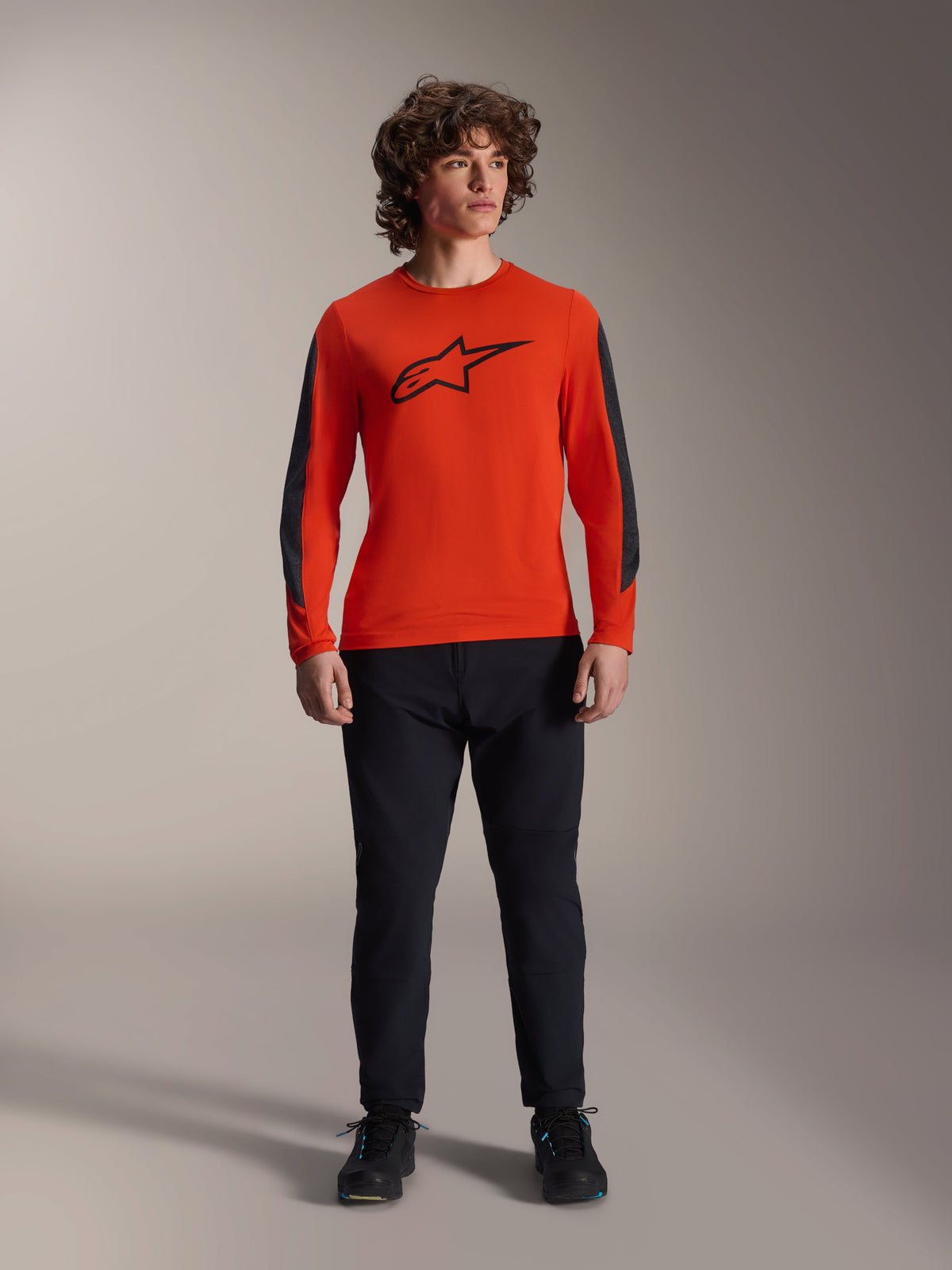Alpinestars A-Dura Insert Astar Jersey - Maniche Lunghe, Spicy Orange con logo Astar nero e pannelli grigio scuro sulle maniche, indossata con pantaloni e scarpe da mountain bike neri, struttura in tessuto resistente per il fuoristrada