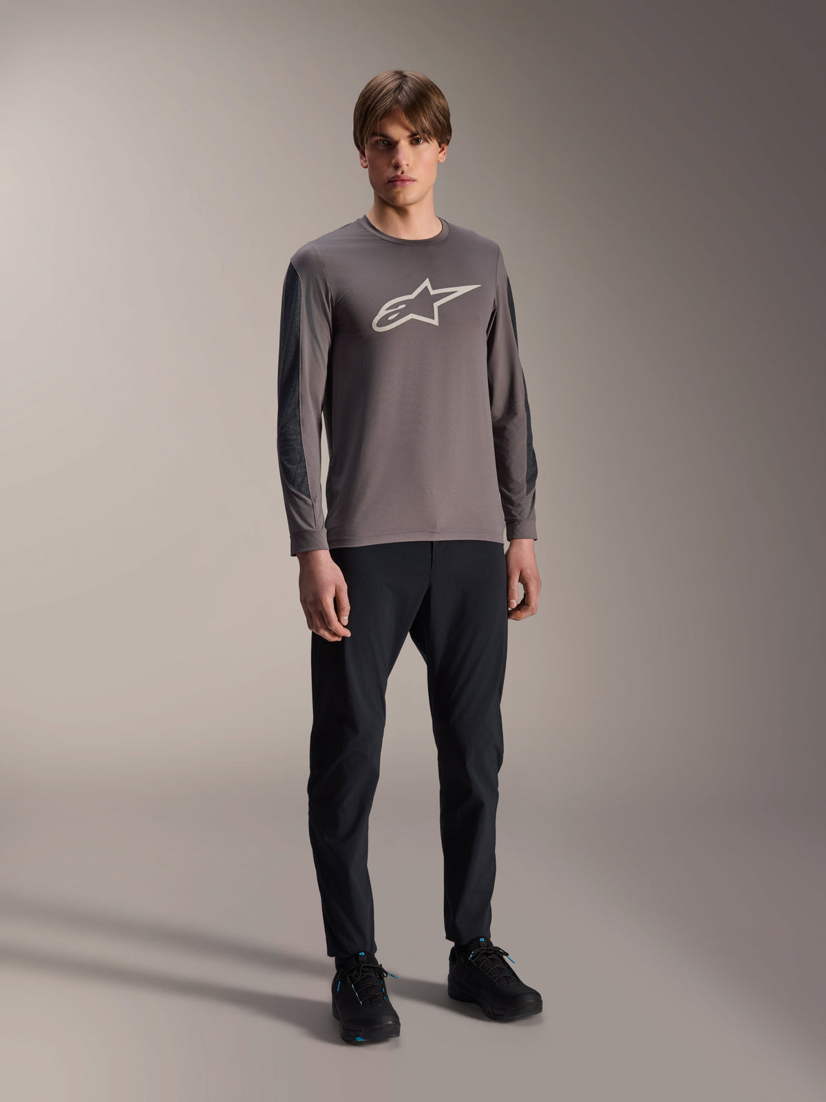 Maglia Alpinestars A-Dura Insert Astar, maglia MTB a maniche lunghe, grigio scuro, con grande logo bianco sul petto, indossata con pantaloni tecnici neri e scarpe nere, abbigliamento per ciclismo off-road