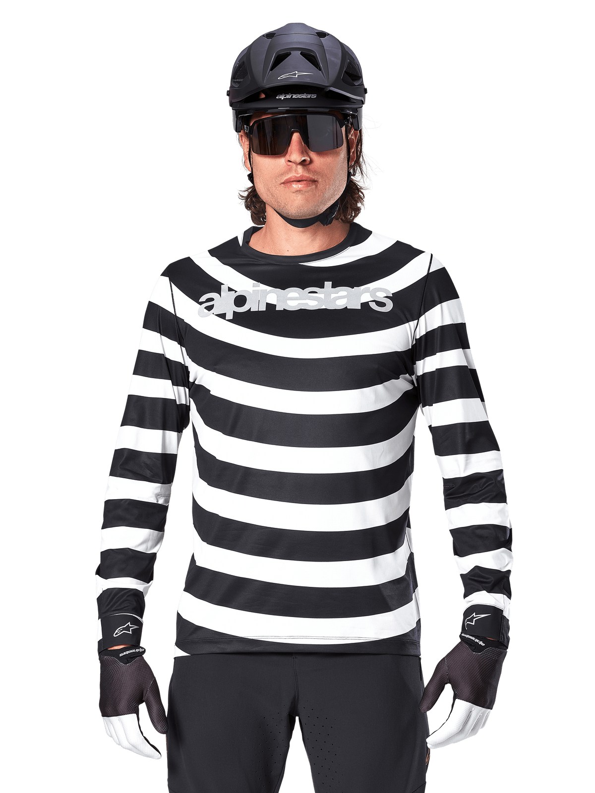 Ciclista uomo con maglia a maniche lunghe Alpinestars A-Aria Oscar, strisce orizzontali bianche e nere, logo Alpinestars riflettente sul petto, abbinata a casco MTB nero, occhiali da ciclismo e guanti tecnici
