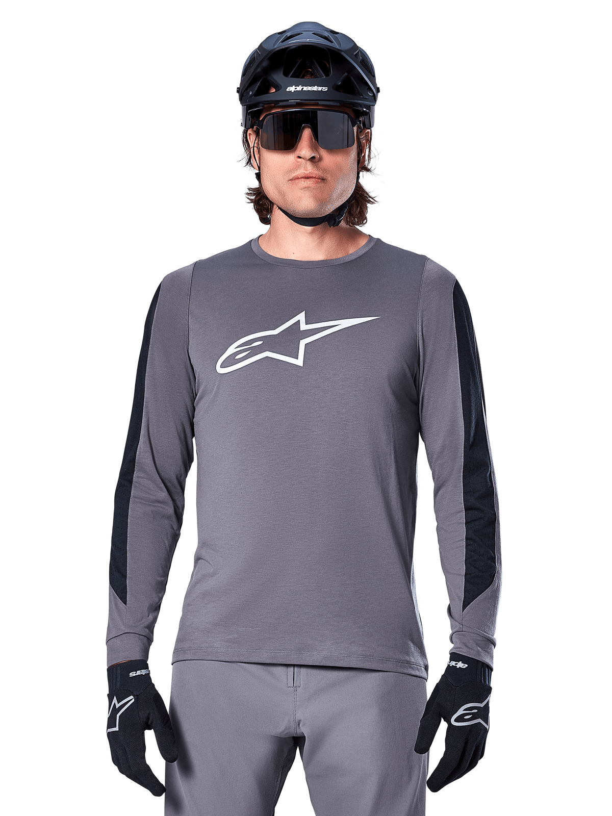 Alpinestars A-Dura Dri Astar Long Sleeve Jersey, maglia a maniche lunghe grigio scuro, con un grande logo Astar bianco sul petto e pannelli in mesh neri sulle braccia, indossata da un ciclista con casco da mountain bike nero e occhiali tecnici, abbigliamento da ciclismo MTB