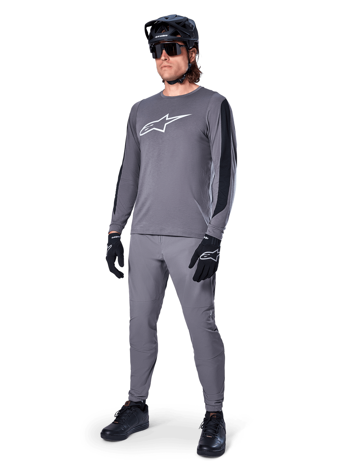 Maglia Alpinestars A-Dura Dri Astar, maglia MTB a maniche lunghe, grigio scuro con logo bianco sul petto, pannelli in mesh neri sulle maniche, indossata con pantaloni grigi coordinati, casco e guanti neri, abbigliamento per mountain bike ad alte prestazioni