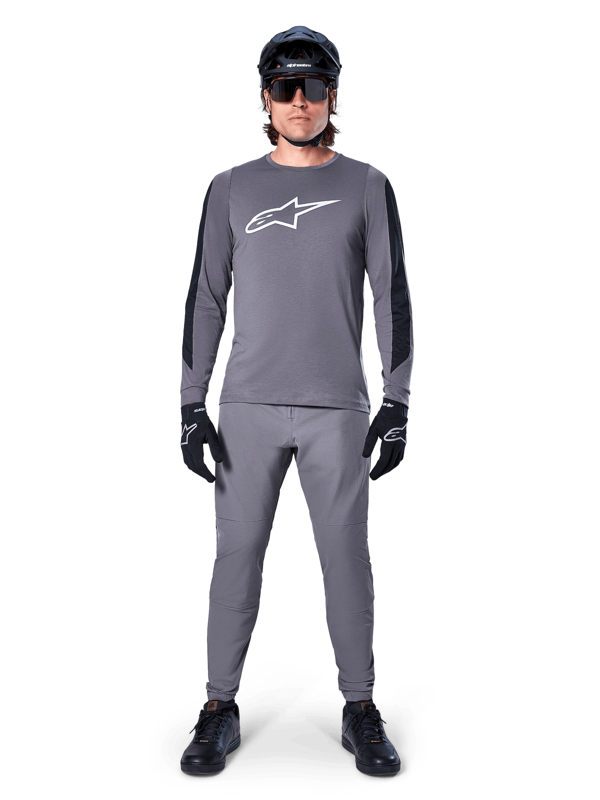 Alpinestars A-Dura Dri Astar Jersey, maglia da MTB a maniche lunghe in grigio scuro, caratterizzata da logo bianco sul petto e pannelli neri sulle maniche, indossata con pantaloni grigi coordinati, casco nero, occhiali da sole e guanti per un outfit completo da ciclismo fuoristrada