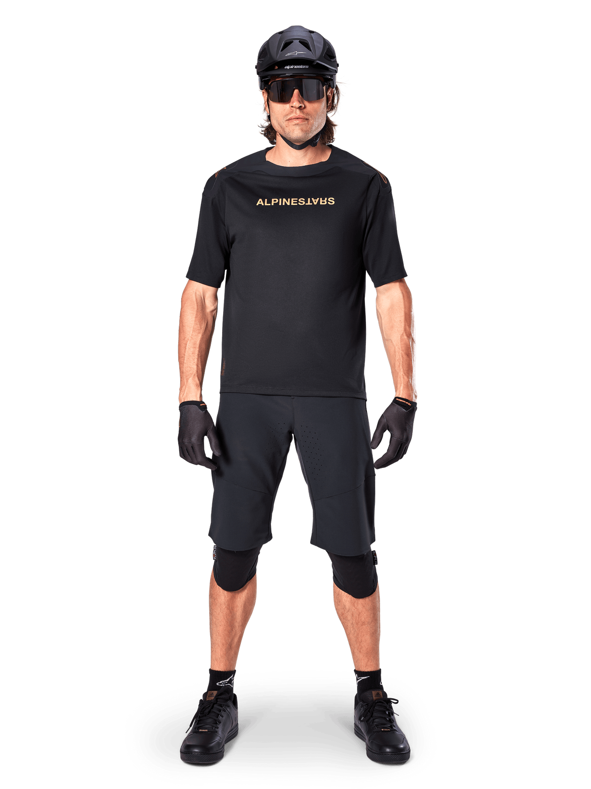 Alpinestars A-Aria Polartec Switch Jersey, maglia MTB a maniche corte, nero con scritte tan, indossata con equipaggiamento da mountain bike nero coordinato comprensivo di casco, pantaloncini e ginocchiere, abbigliamento tecnico da ciclismo fuoristrada