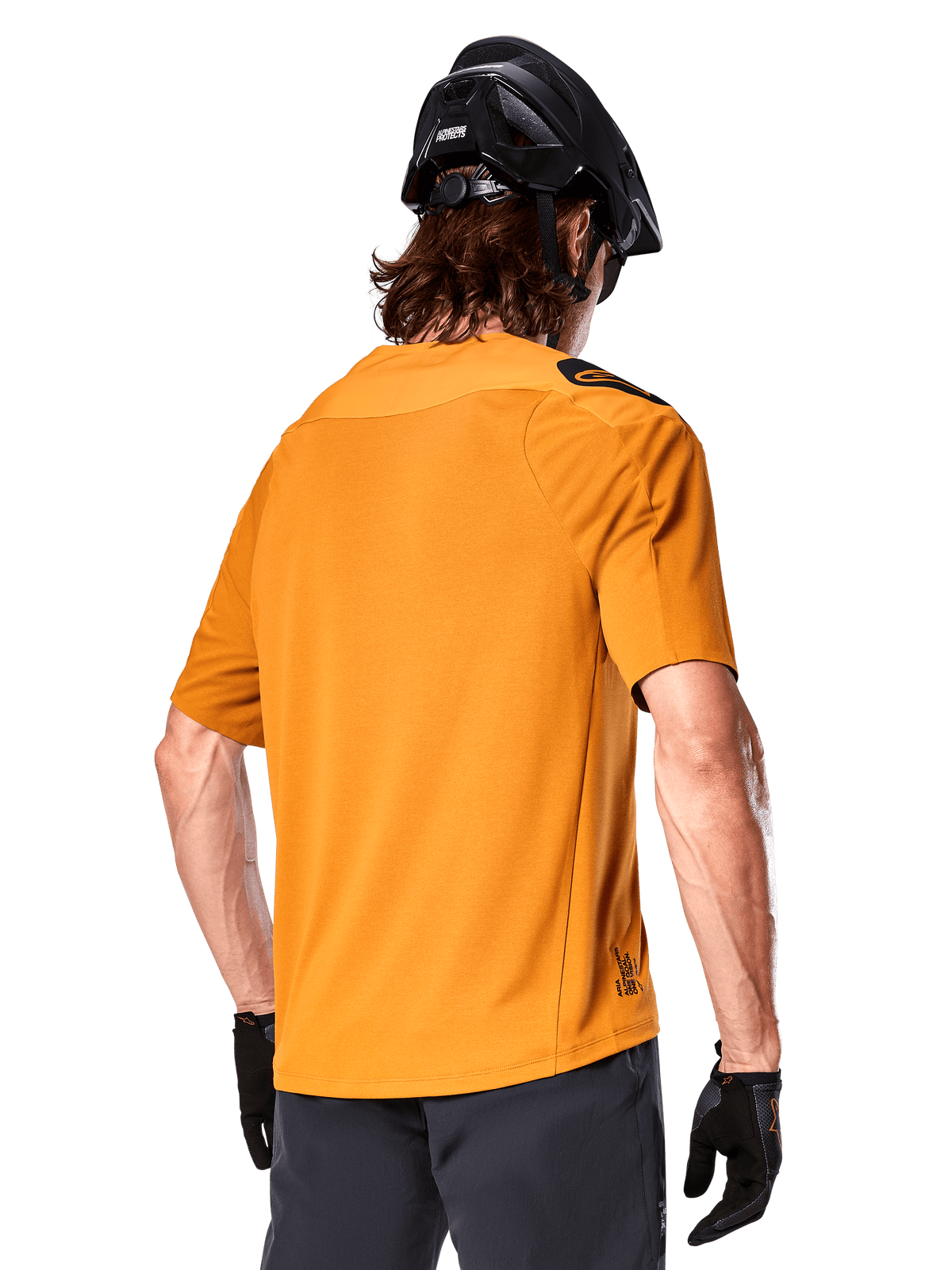Maglia Alpinestars A-Aria Polartec Switch, maglia da MTB a maniche corte, oro scuro, vista posteriore con vestibilità performante, indossata con casco nero e pantaloncini grigi, abbigliamento da trail riding resistente e traspirante