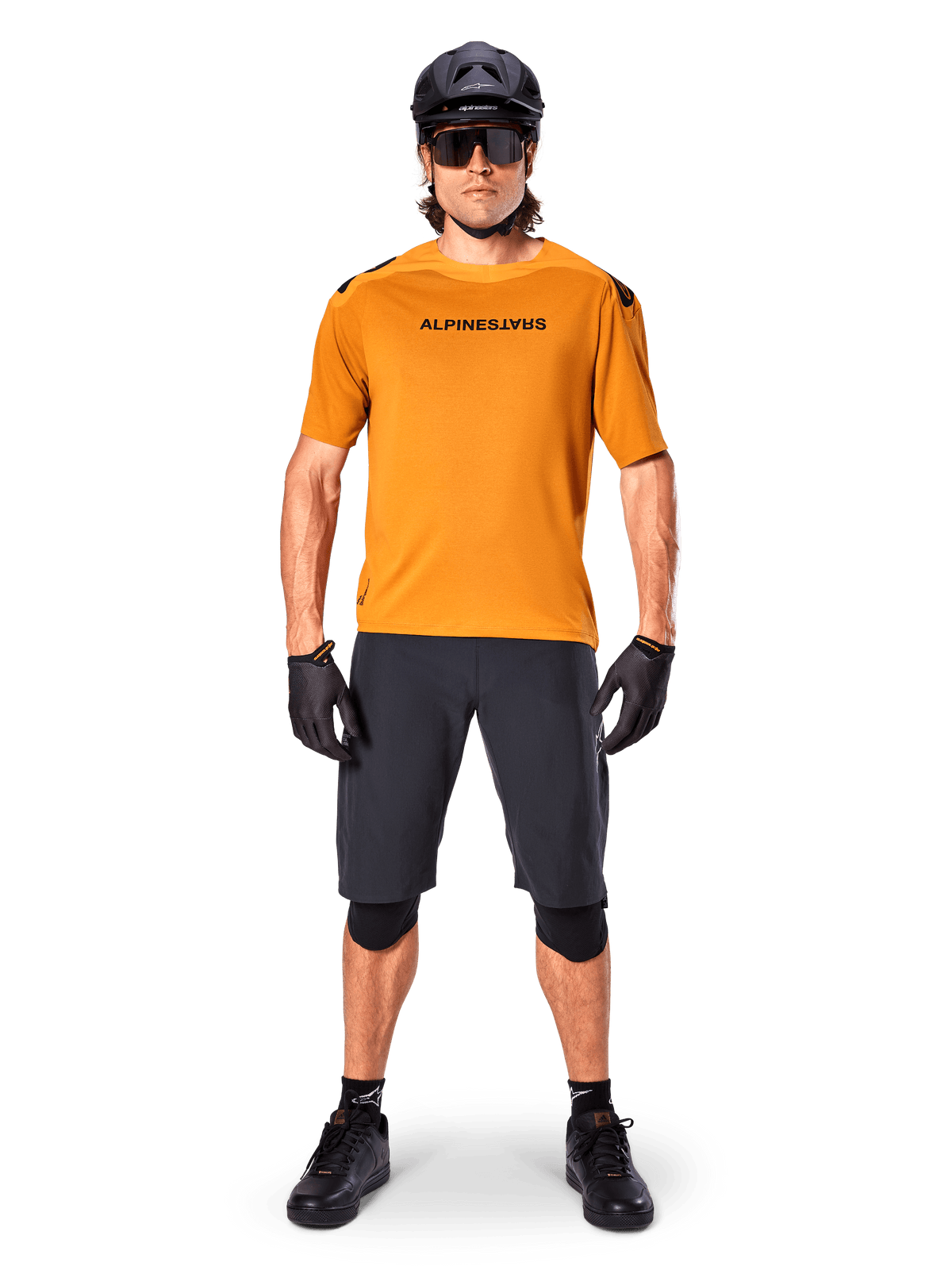 Ciclista uomo che indossa la maglia a maniche corte Alpinestars A-Aria Polartec Switch in Dark Gold, abbinata a pantaloncini da MTB neri, casco, occhiali da sole e guanti, abbigliamento professionale da mountain bike
