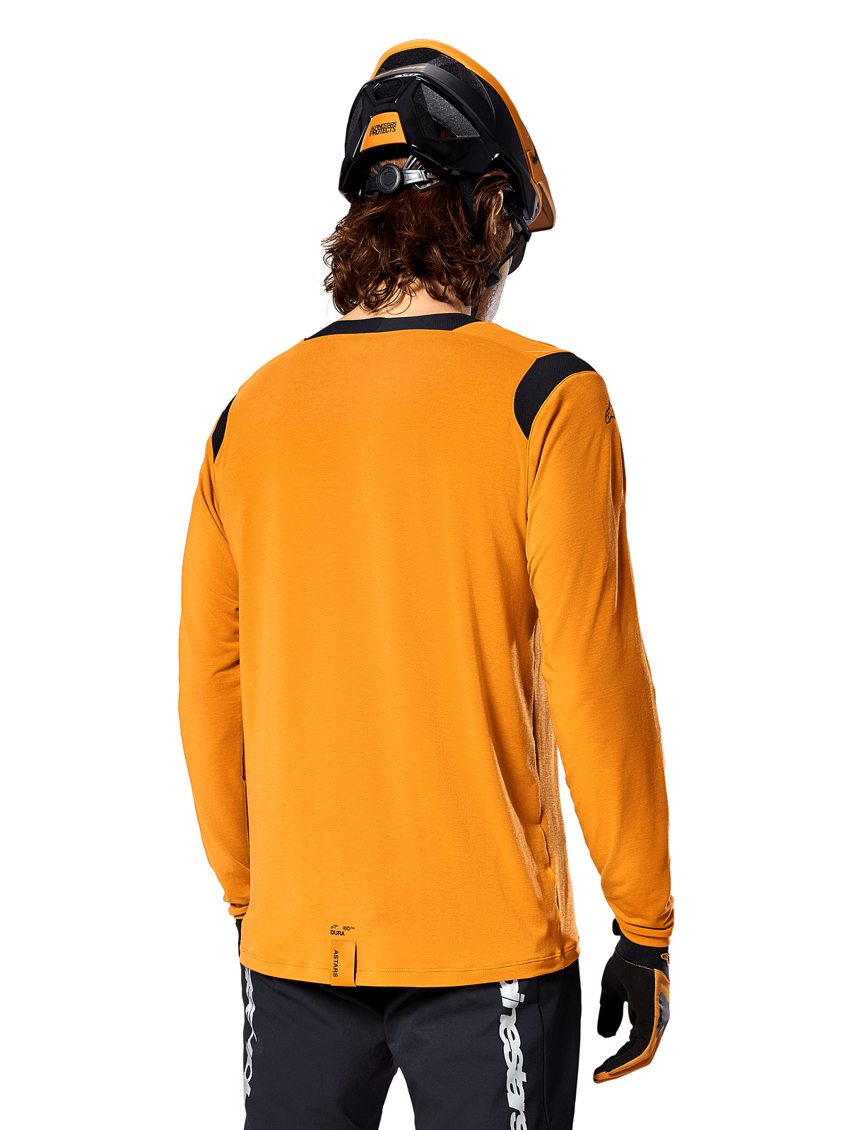 Alpinestars A-Dura Dri Wool Long Sleeve Jersey in Dark Gold, vista posteriore di un ciclista con casco da mountain bike e guanti, con pannelli in rete nera sulle spalle e coda più lunga, abbigliamento tecnico da ciclismo per trail riding